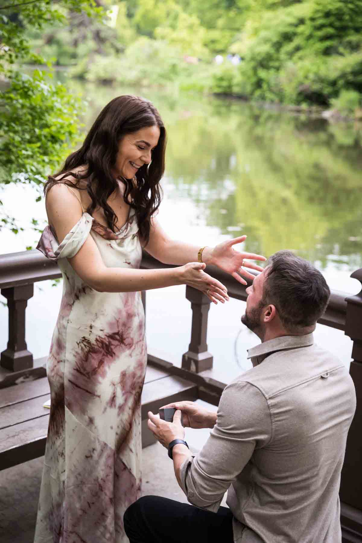 Man down on one knee asking girl to marry him on dock during a Central Park surprise proposal