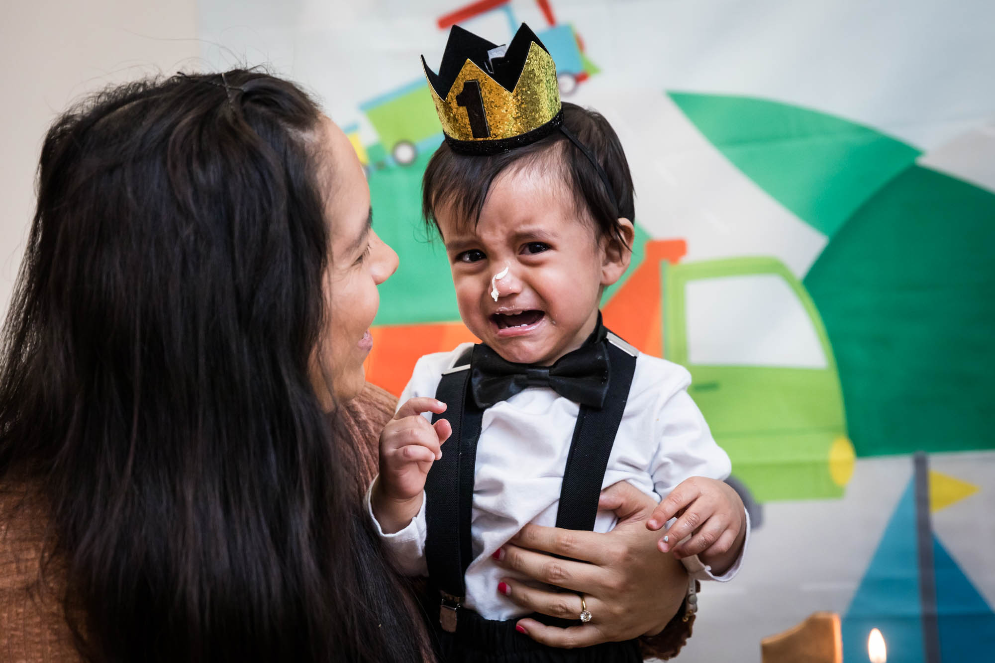 Mother holding crying little boy wearing gold crown and black bow tie for an article on cake smash tips