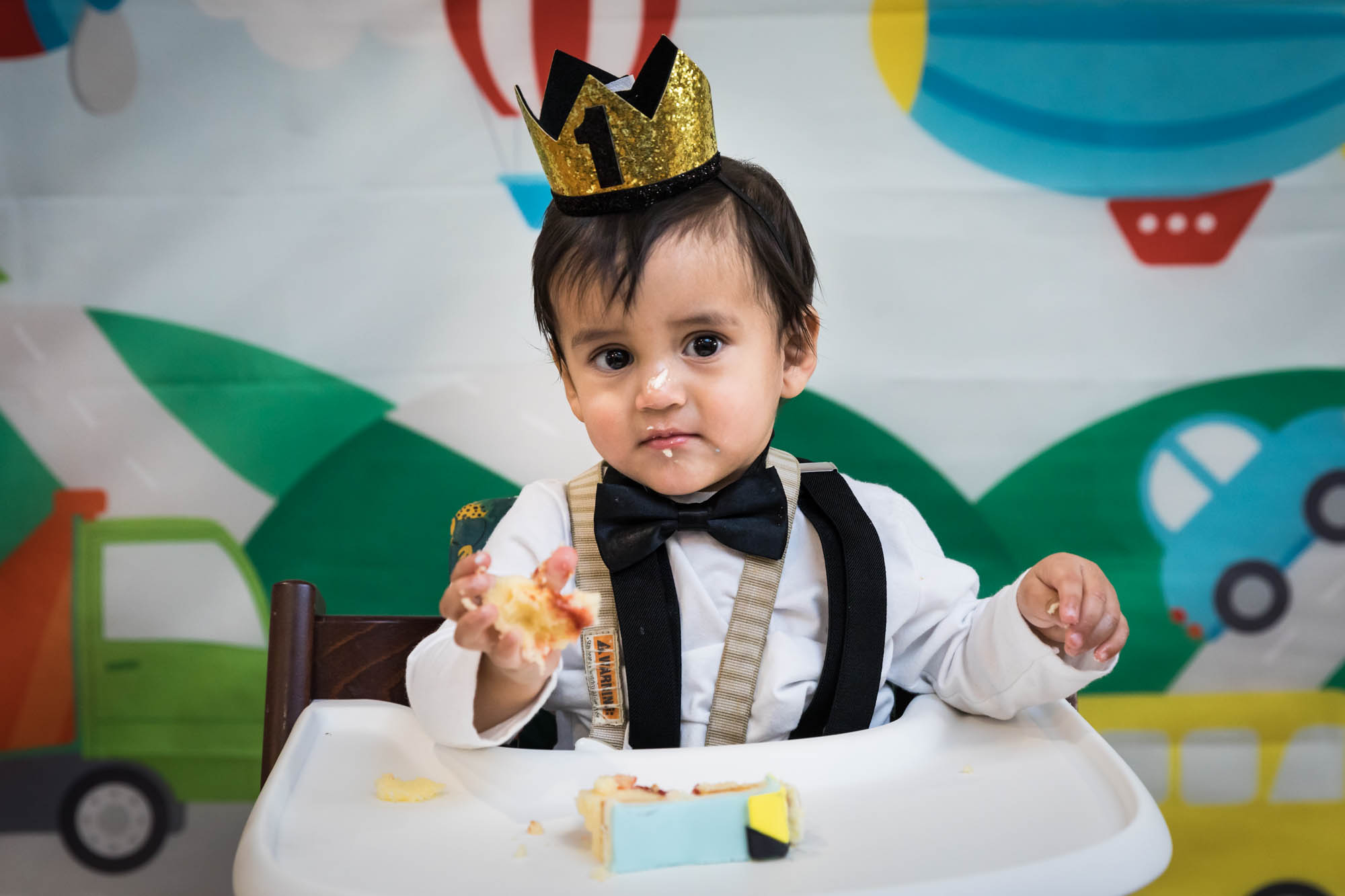 Little boy sitting in high chair wearing gold crown and black bow tie for an article on cake smash tips
