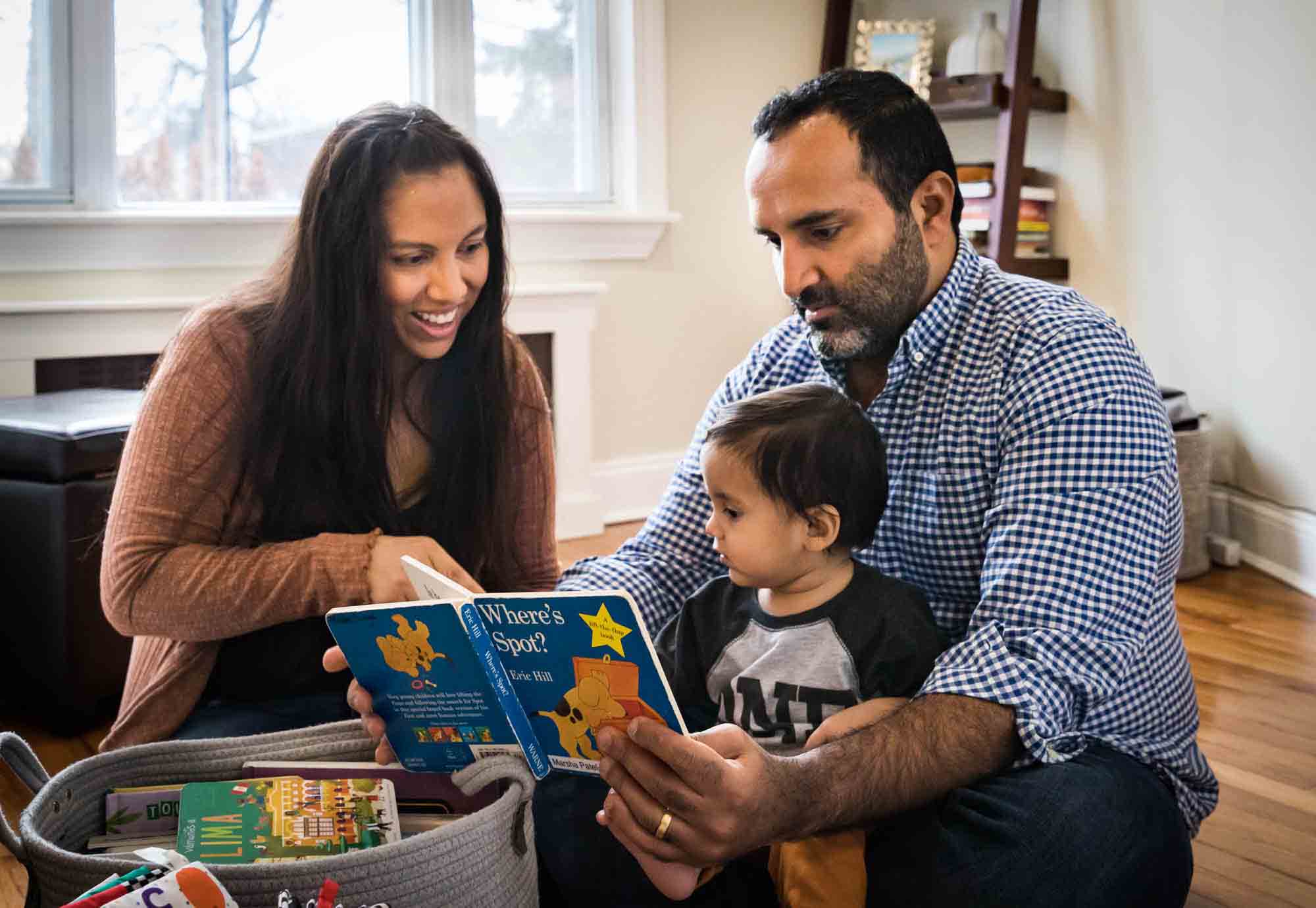 Parents sitting on wooden floor in front of window reading a book to a little boy for an article on cake smash tips