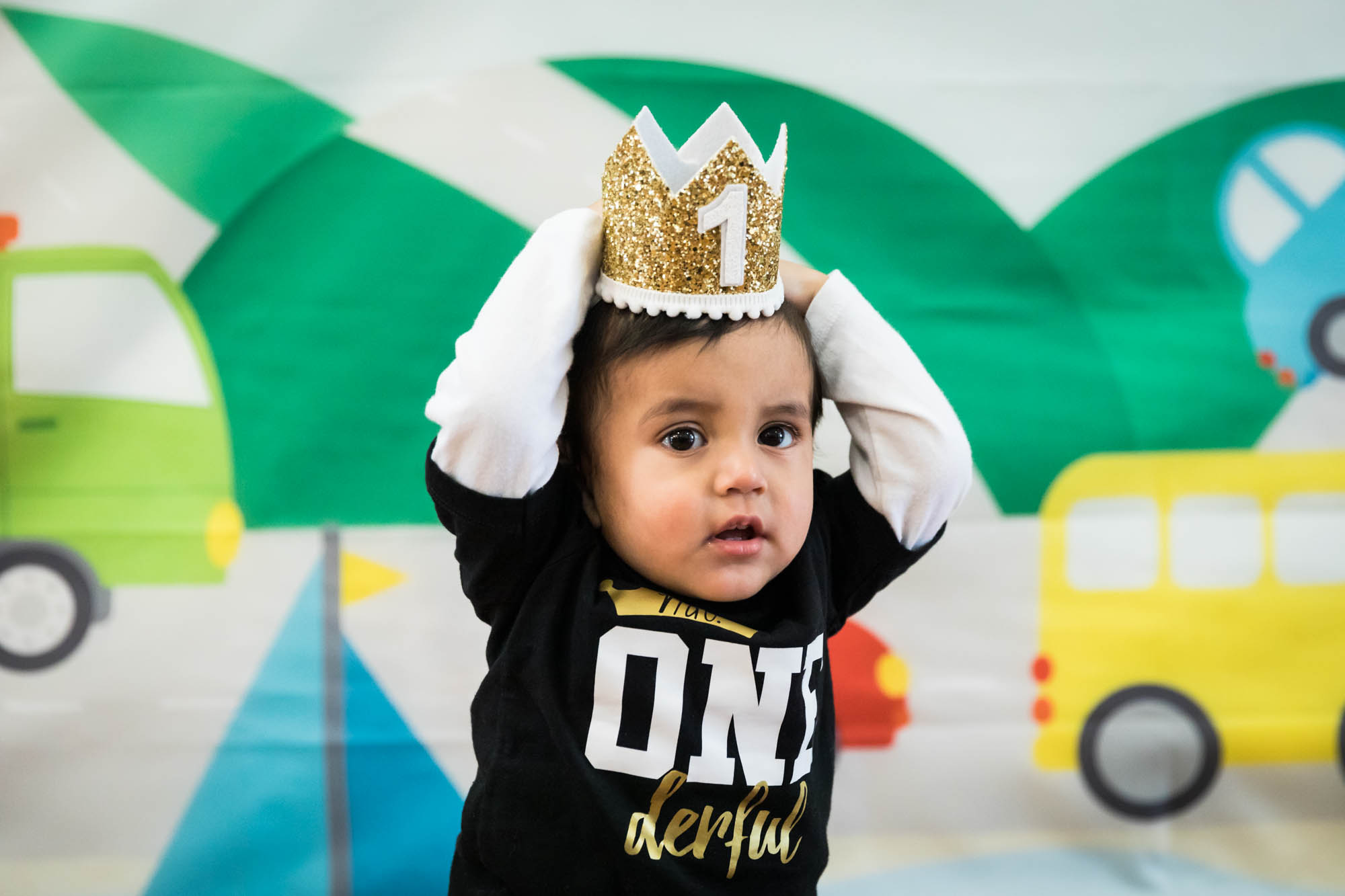 Little boy wearing black t-shirt and clutching gold crown on his head in front of colorful background during a Queens family portrait