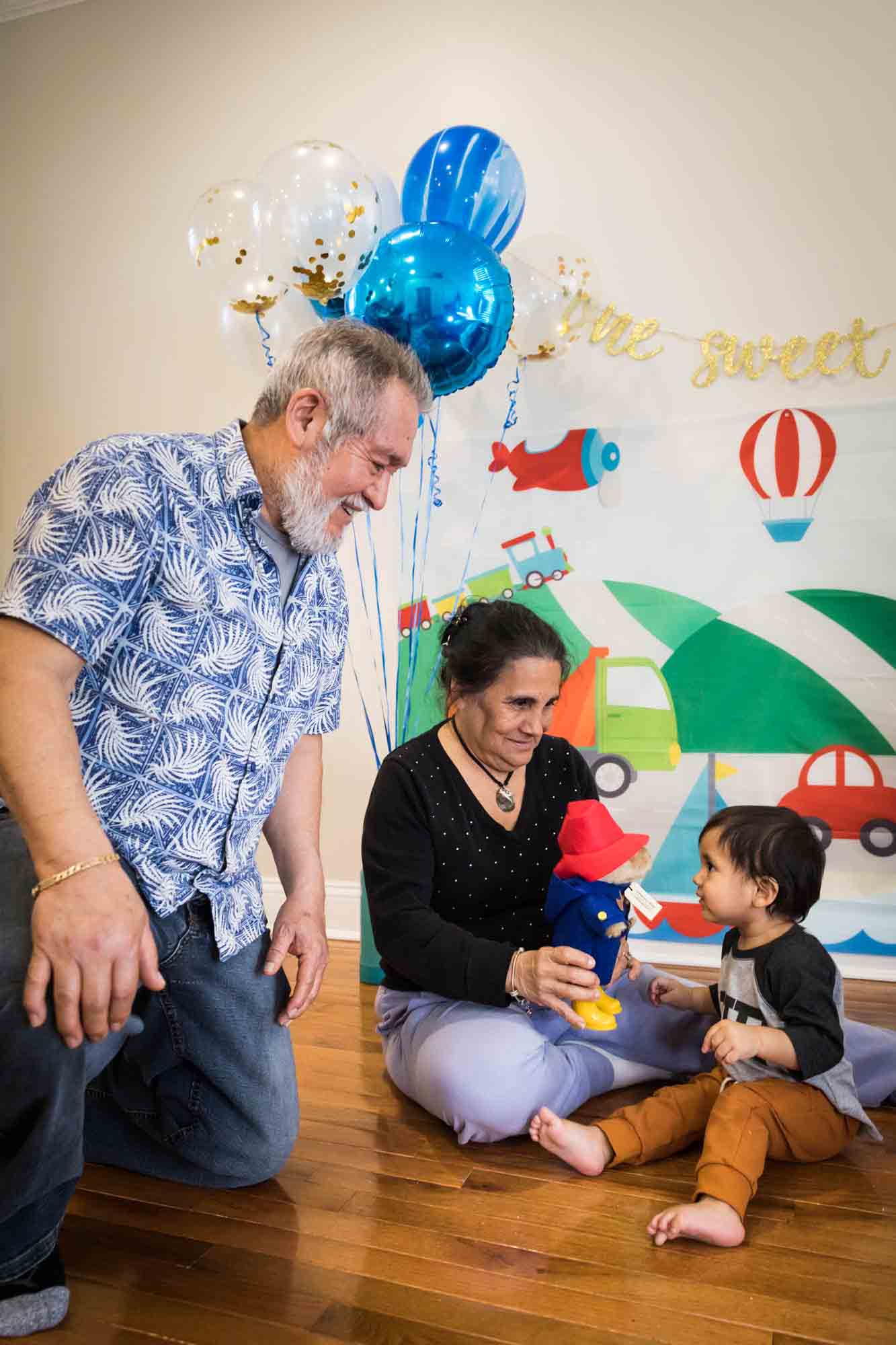 Grandparents showing a teddy bear to little boy on a wooden floor for an article on cake smash tips
