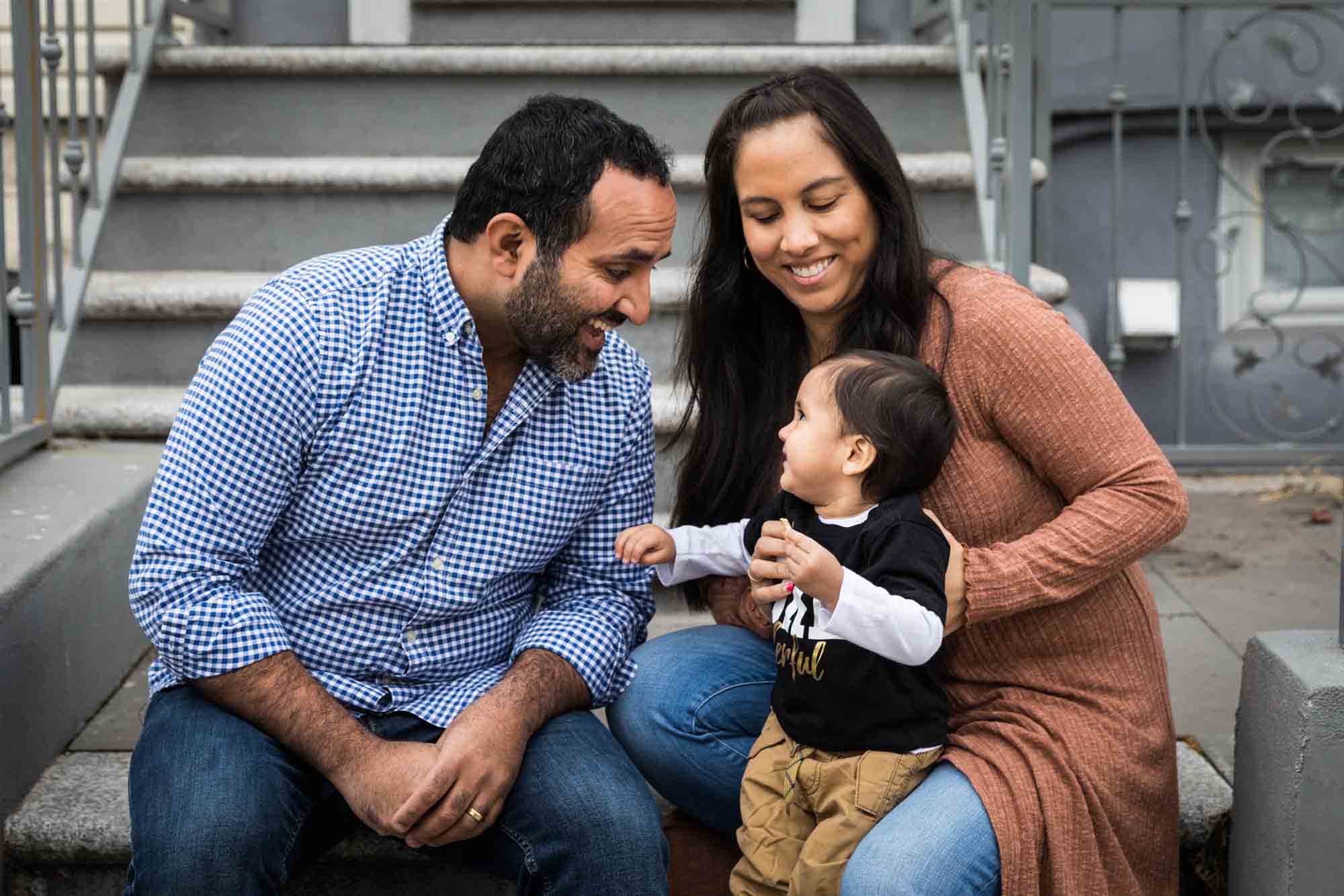 Mother and father playing with little boy on steps of an apartment during a Queens family portrait