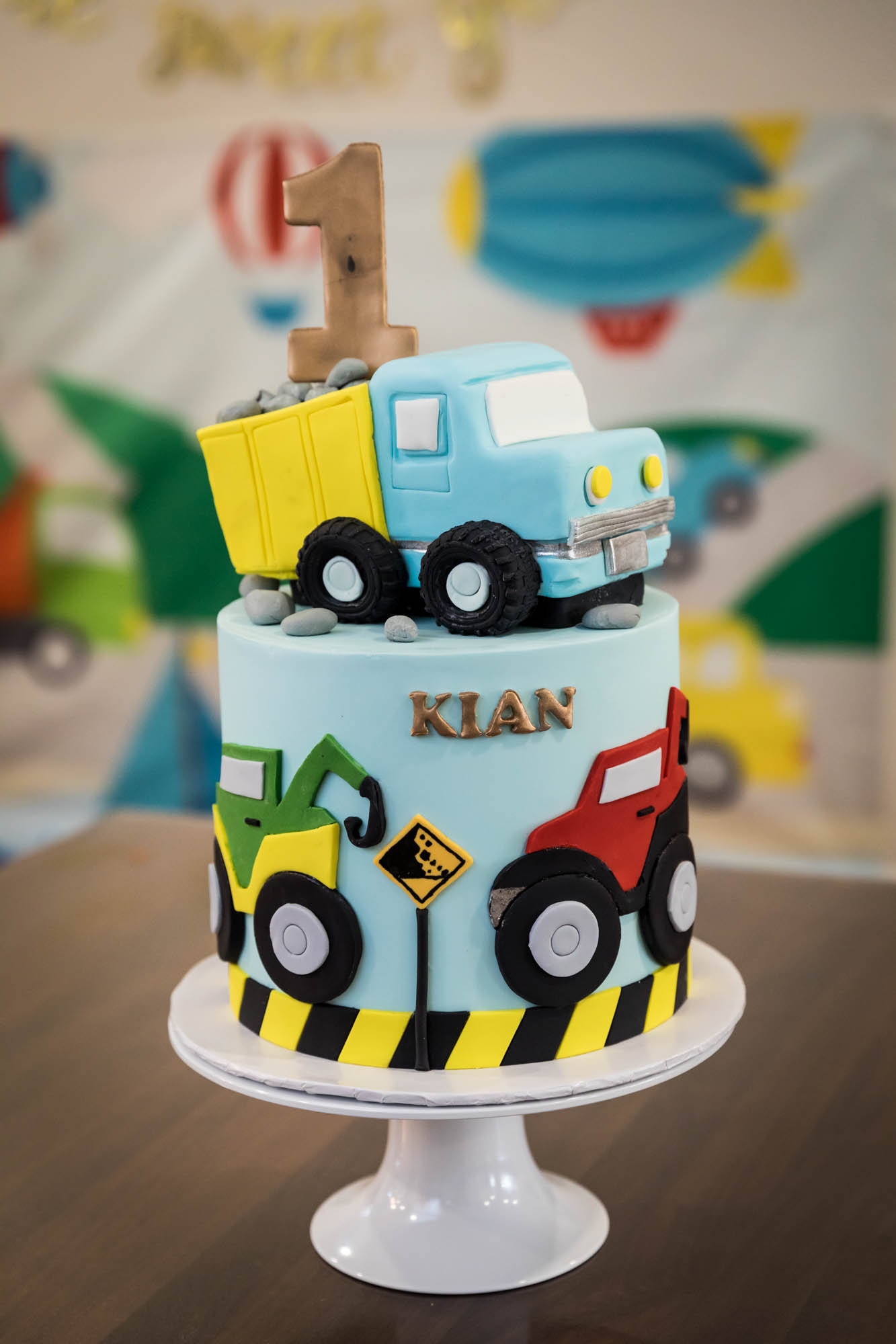 Truck-themed, colorful cake sitting on pedestal on wooden table