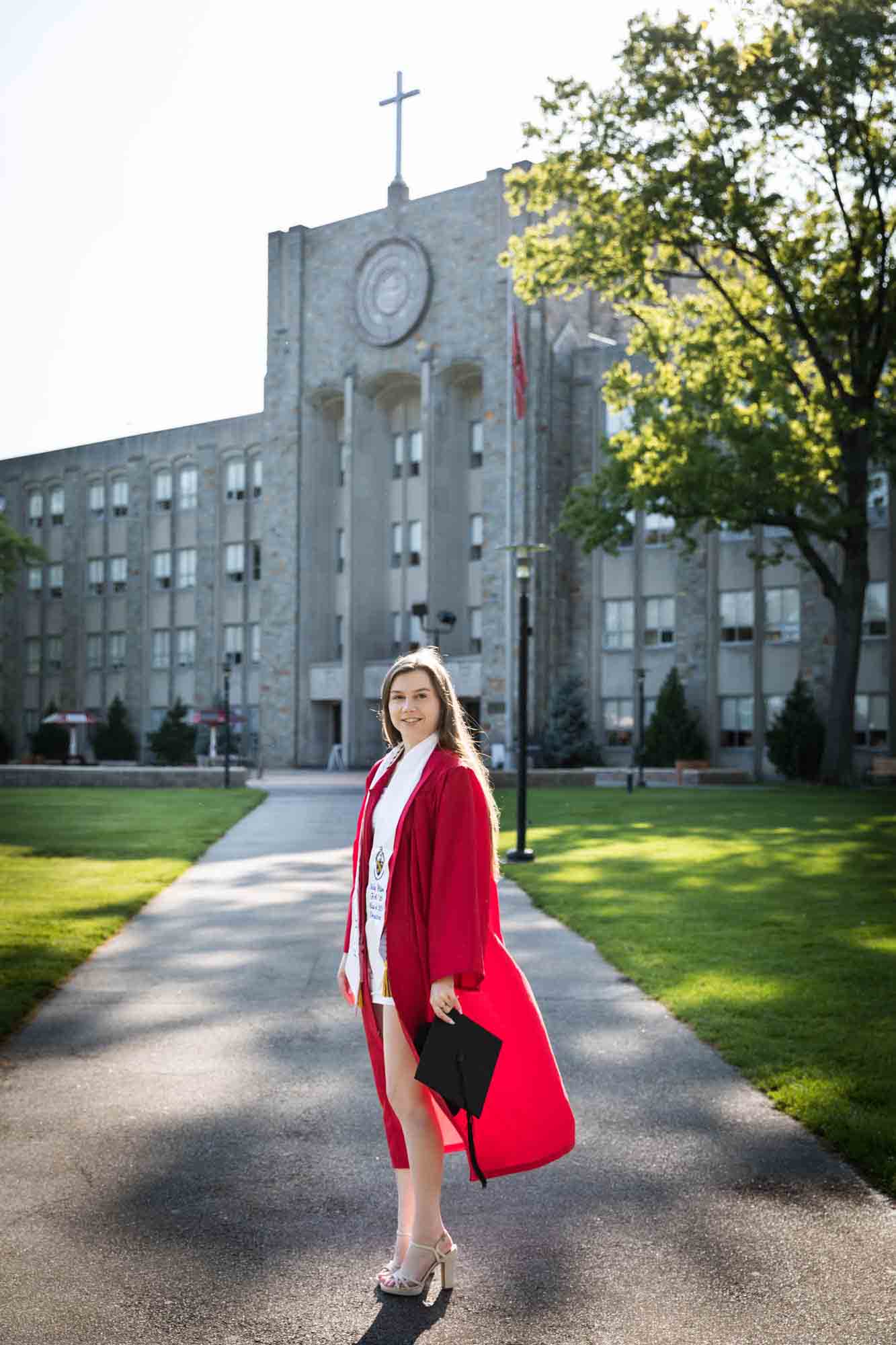 Female graduate wearing red robe and white sash holding cap during a St. John’s University graduate portrait session