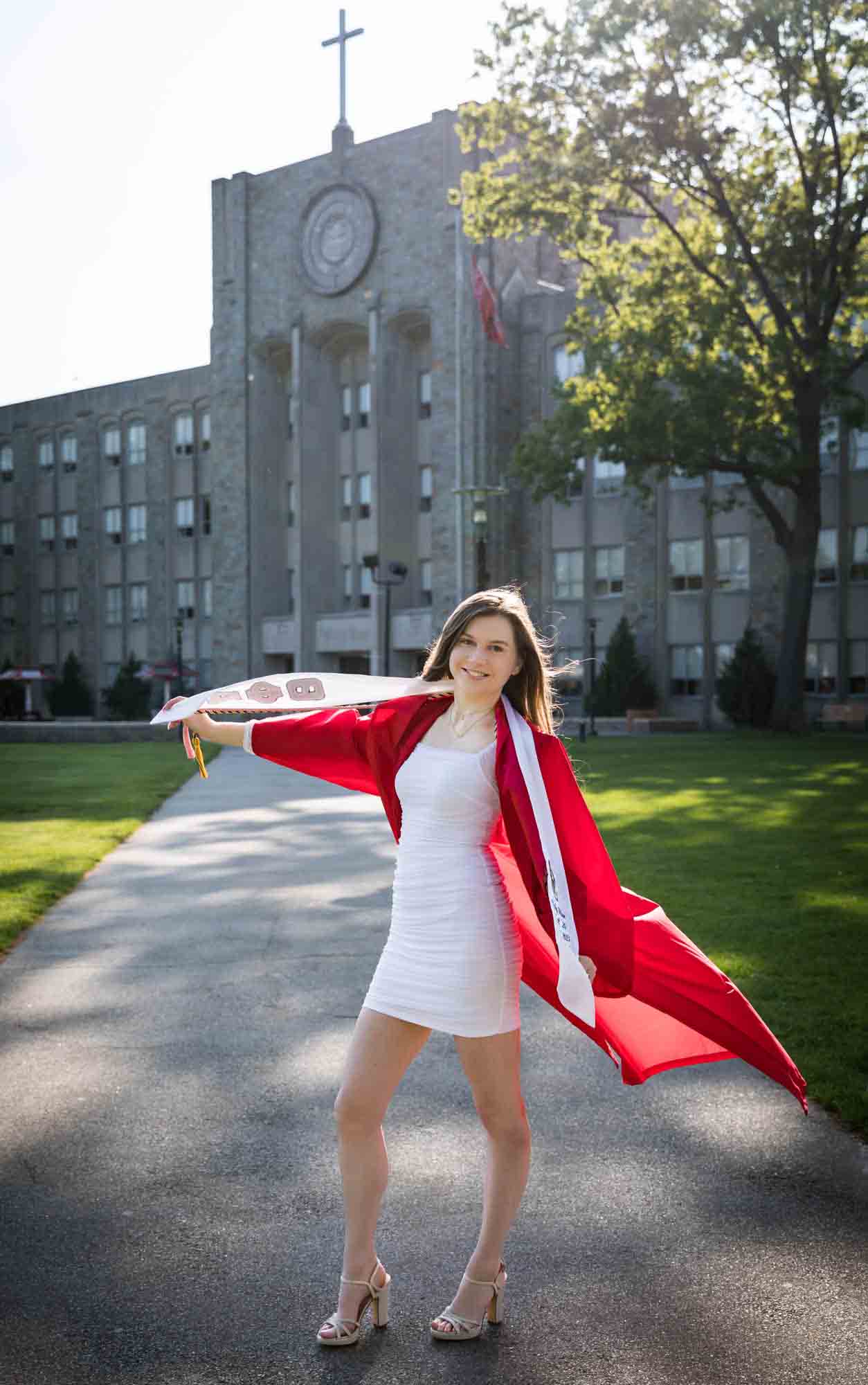 Female graduate wearing red robe and white sash holding white sashes during a St. John’s University graduate portrait session