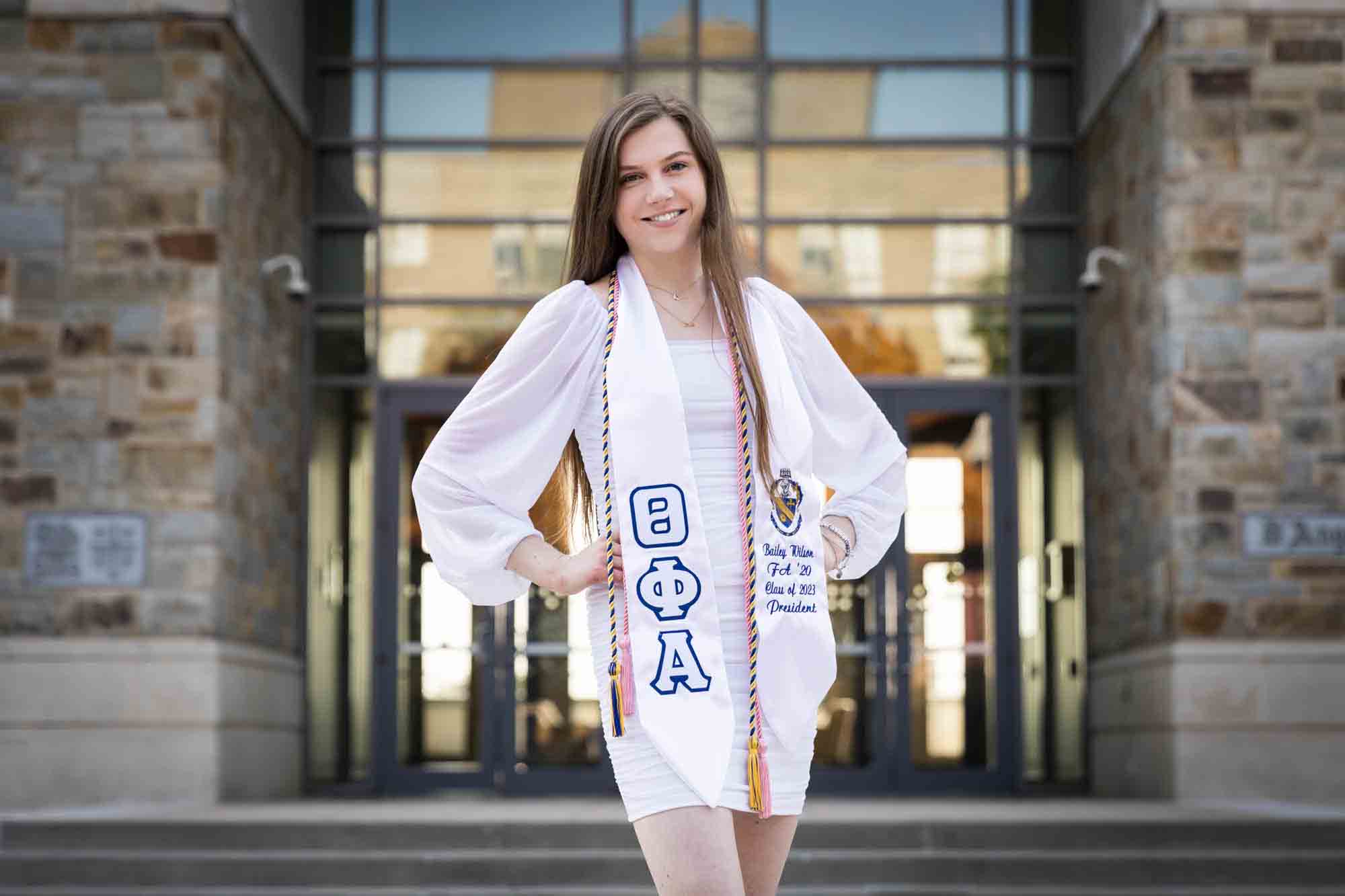 Female graduate wearing white dress with hands on hips during a St. John’s University graduate portrait session