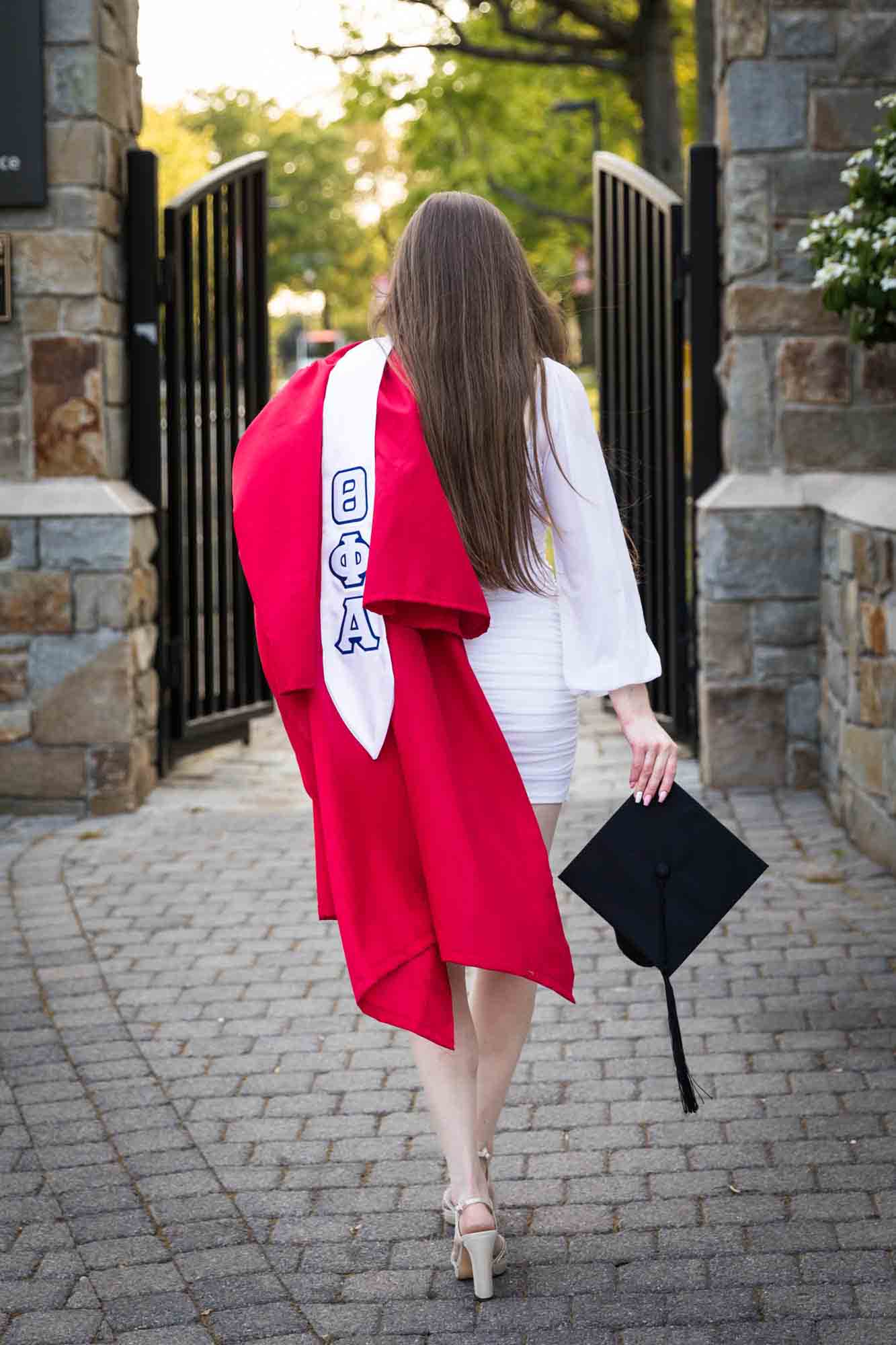 Female graduate holding red robe over shoulder and cap in hand during a St. John’s University graduate portrait session