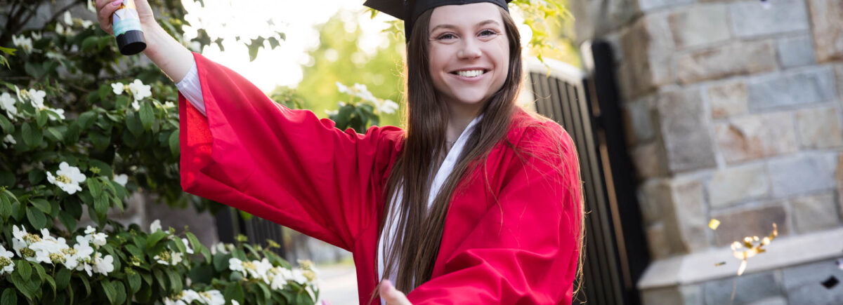 Female graduate wearing red robe and cap releasing confetti for an article on graduation portrait photo tips