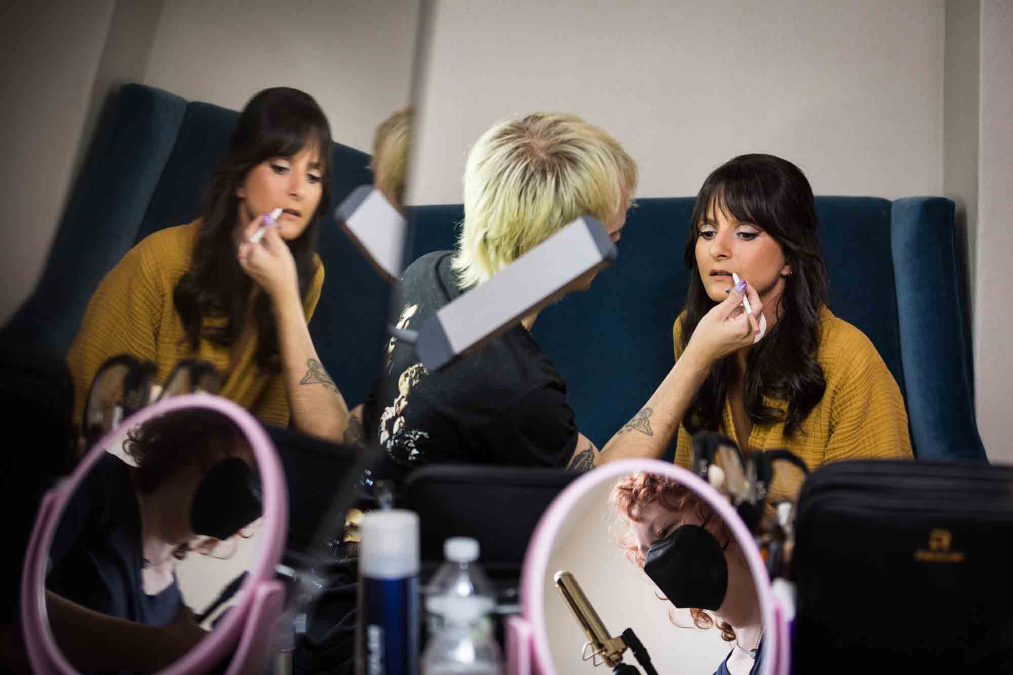 Reflection of makeup artist putting lipstick on bride waring yellow robe