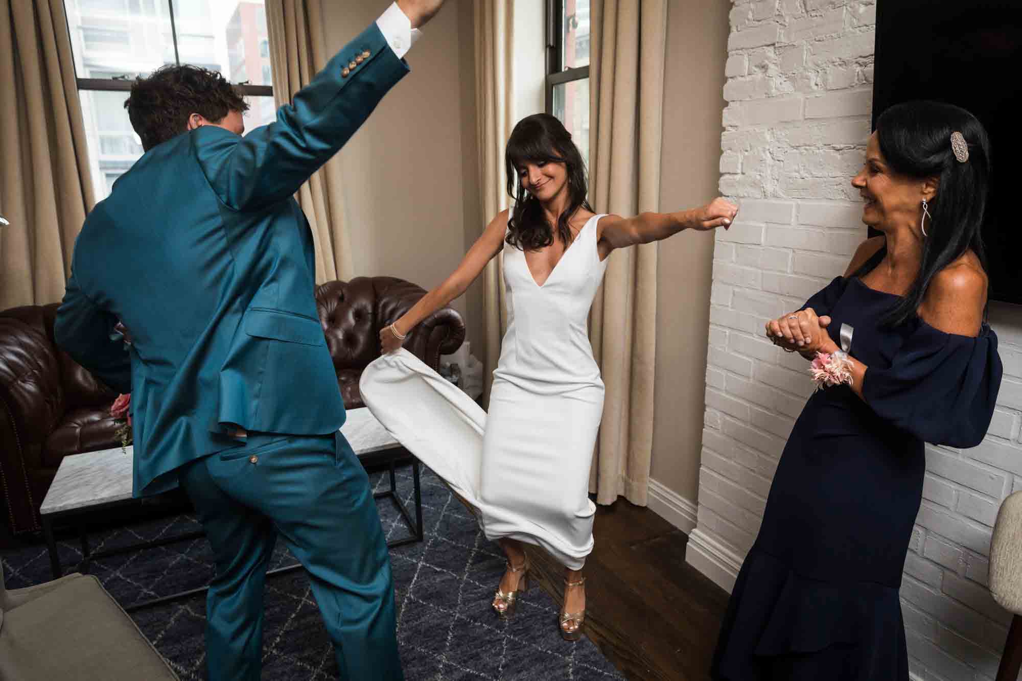 Bride dancing with mother and brother wearing blue suit in hotel room