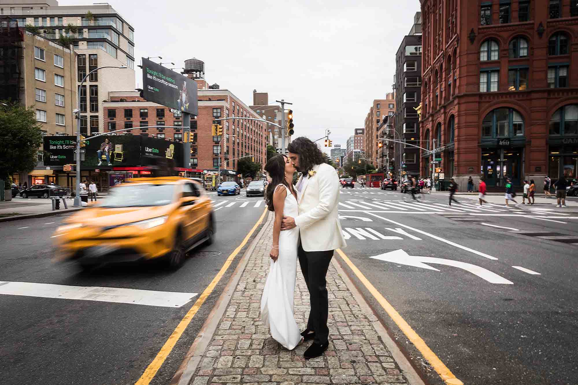Bride and groom kissing in middle of road with taxi speeding past