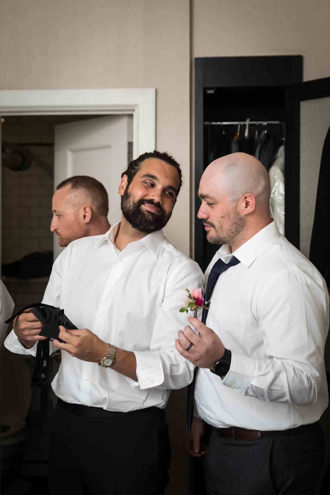 Groom smiling with groomsman holding flowers in hotel room