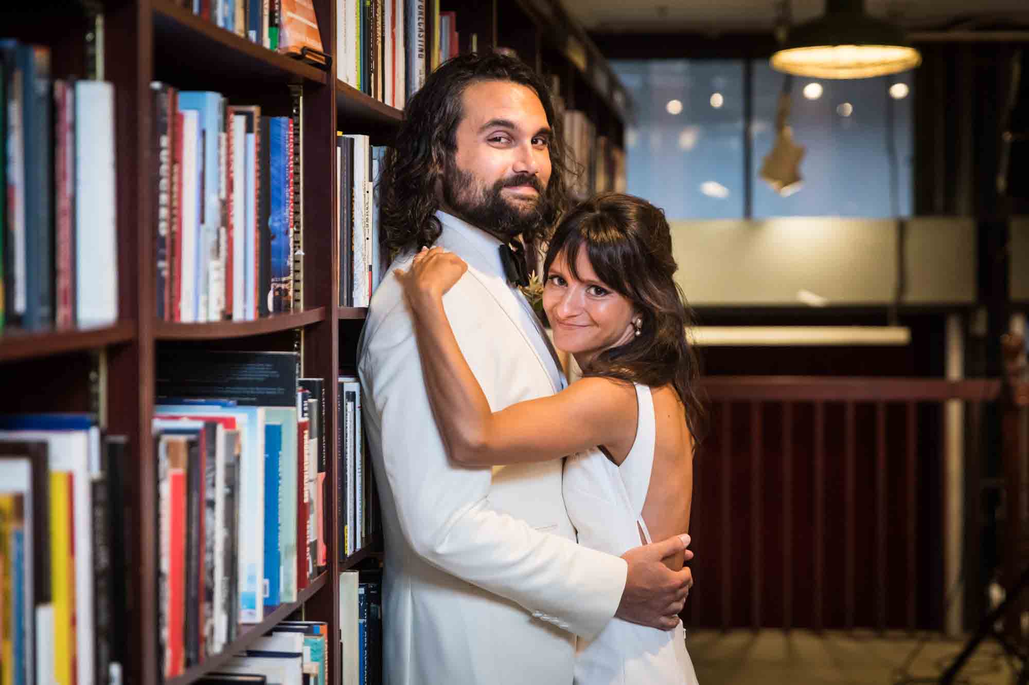 Bride and groom hugging while leaning against bookcase at a Housing Works wedding