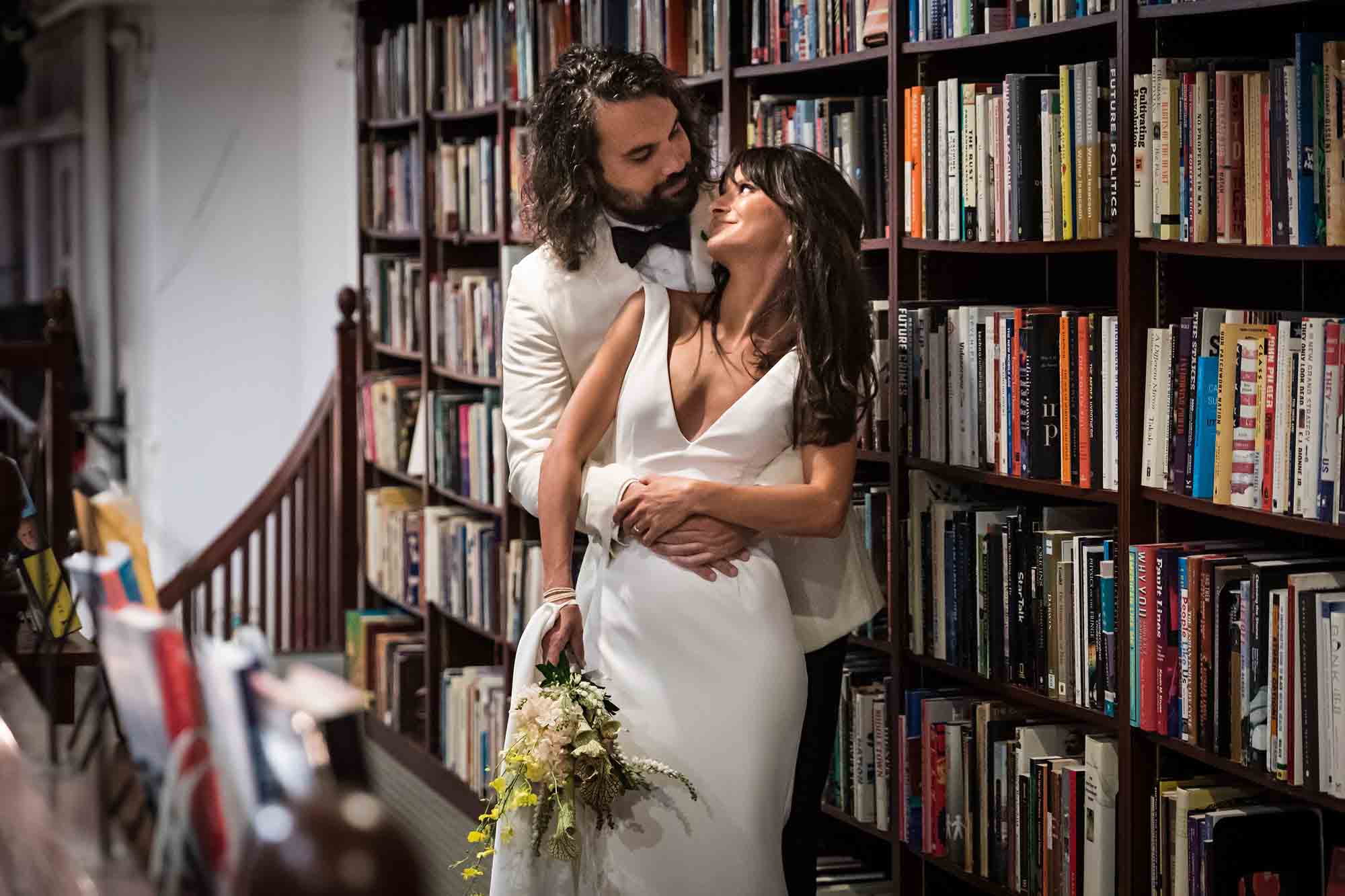 Bride and groom looking at each other while leaning against bookcase at a Housing Works wedding
