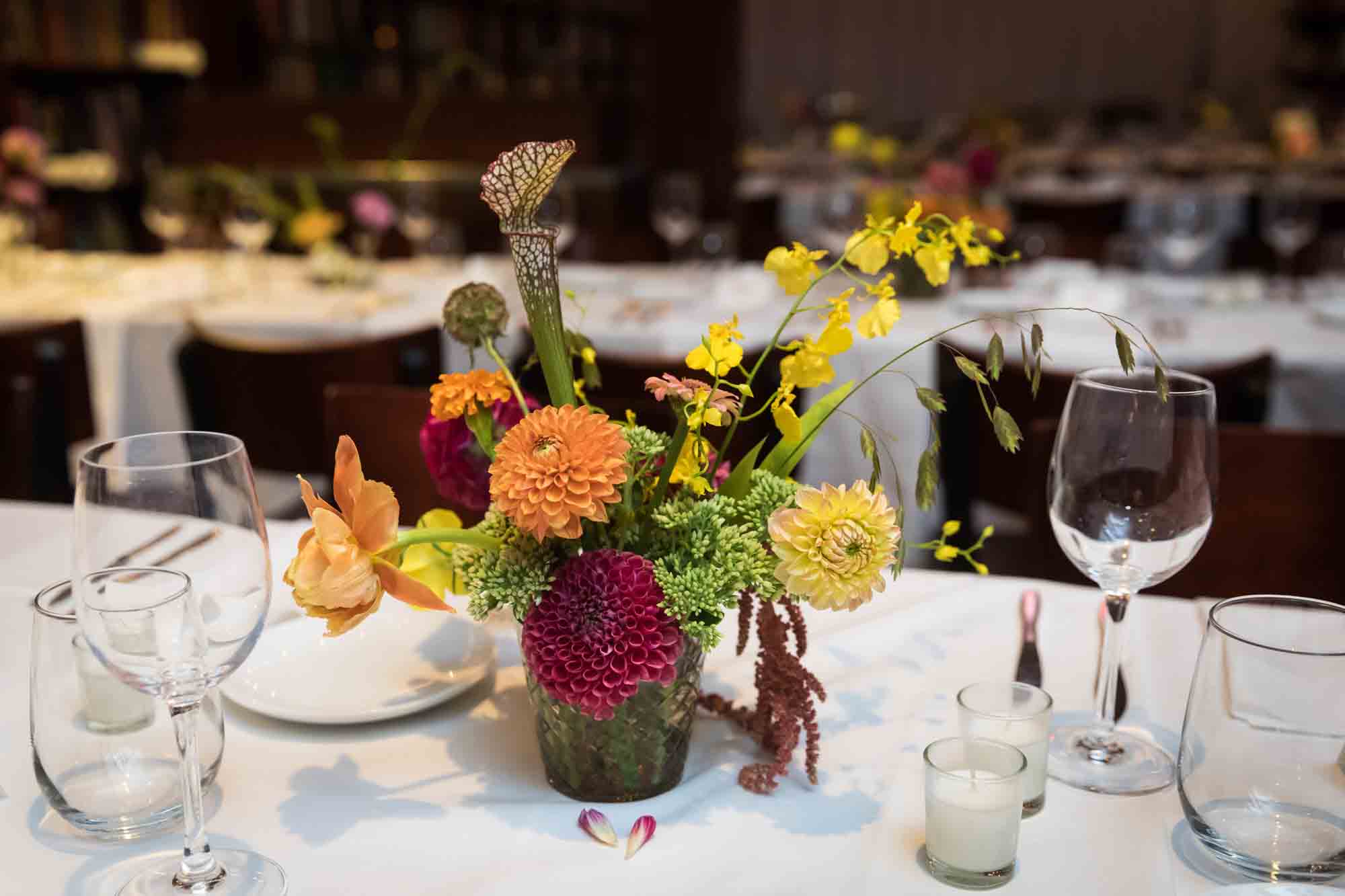 Table with colorful floral arrangement surrounded by glasses and small candles at a Housing Works wedding
