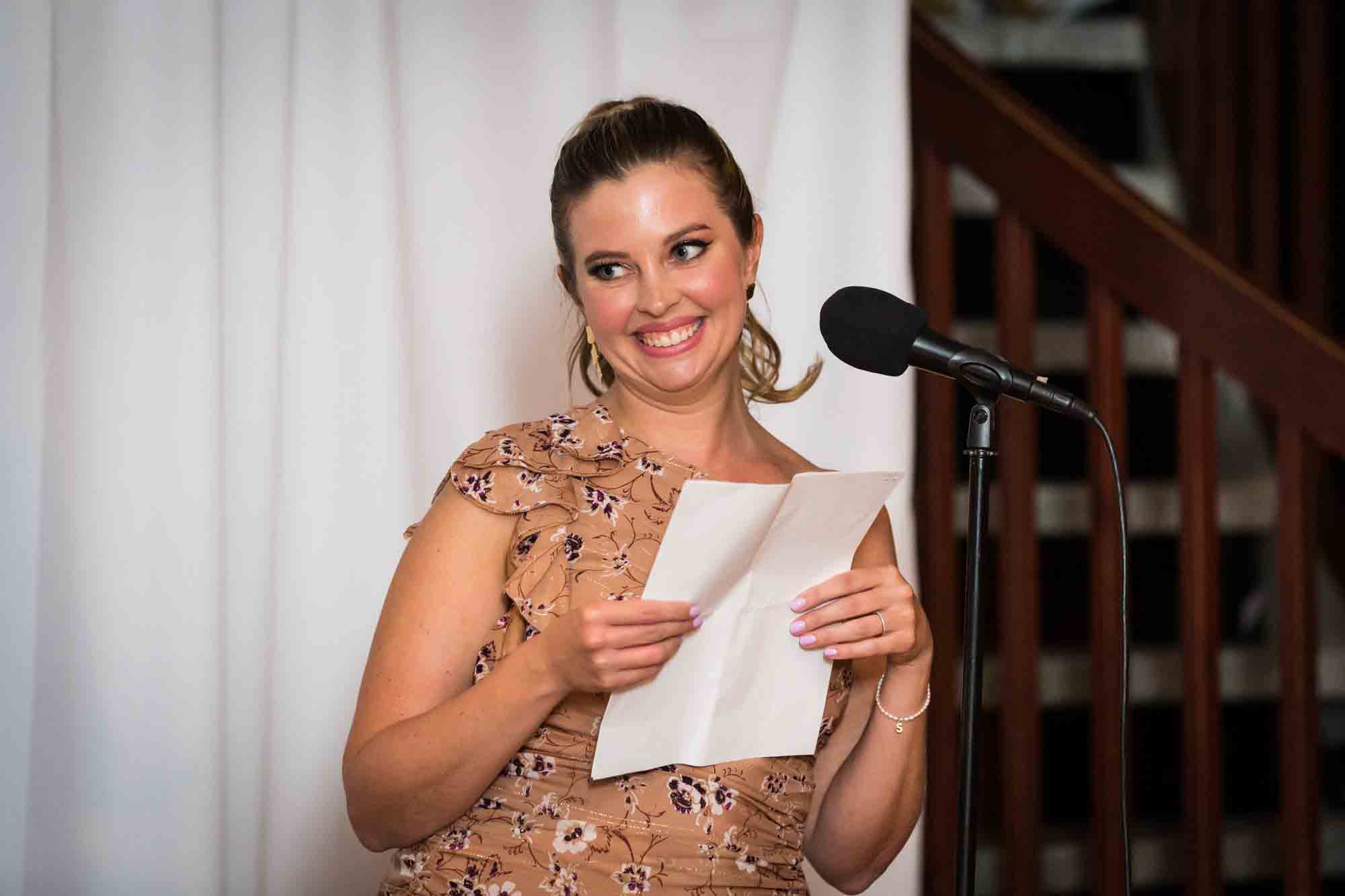 Bridesmaid wearing brown floral dress giving speech in front of microphone during a Housing Works wedding