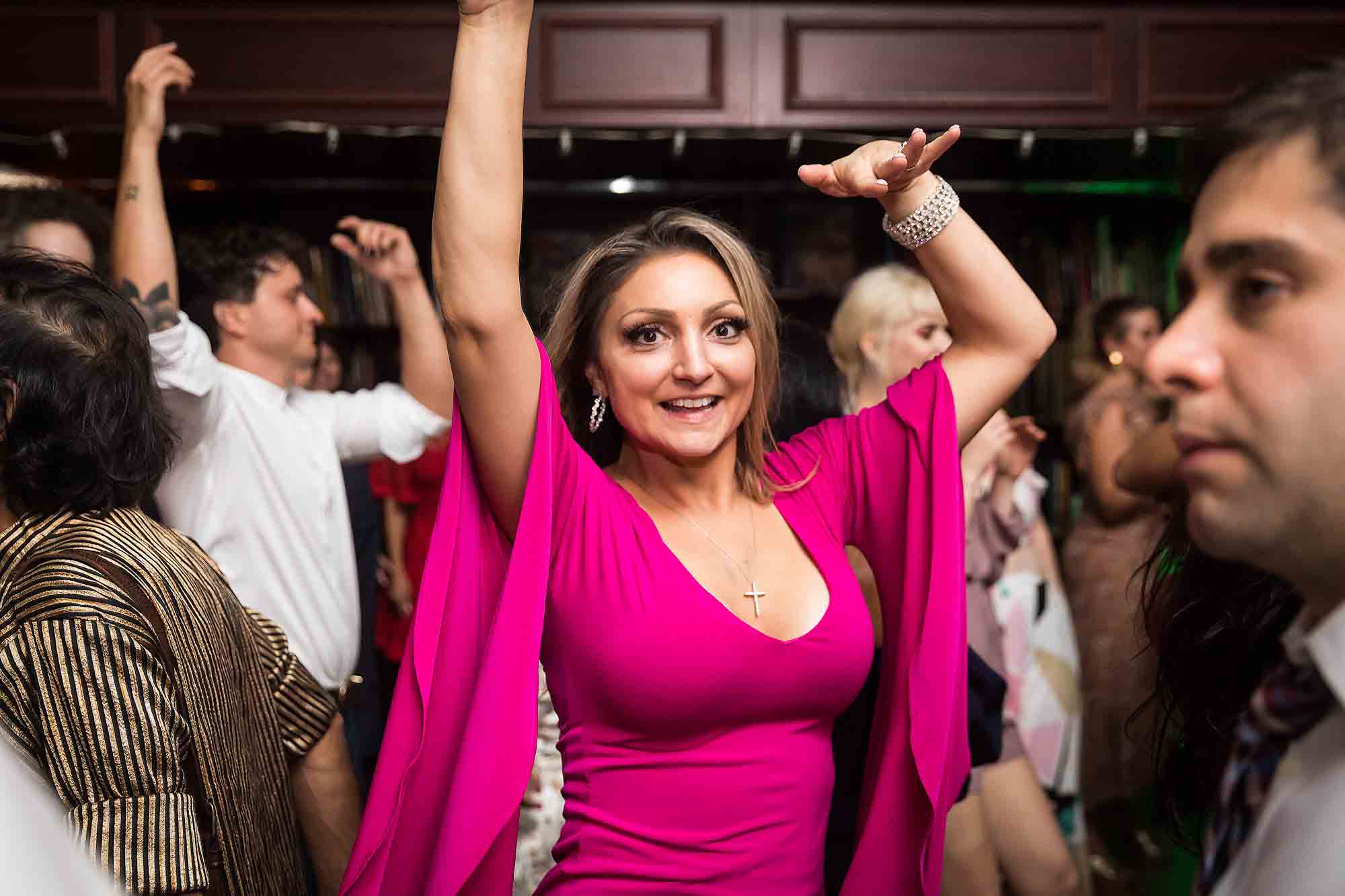 Woman wearing pink dress with long sleeves dancing with arms up at a Housing Works wedding