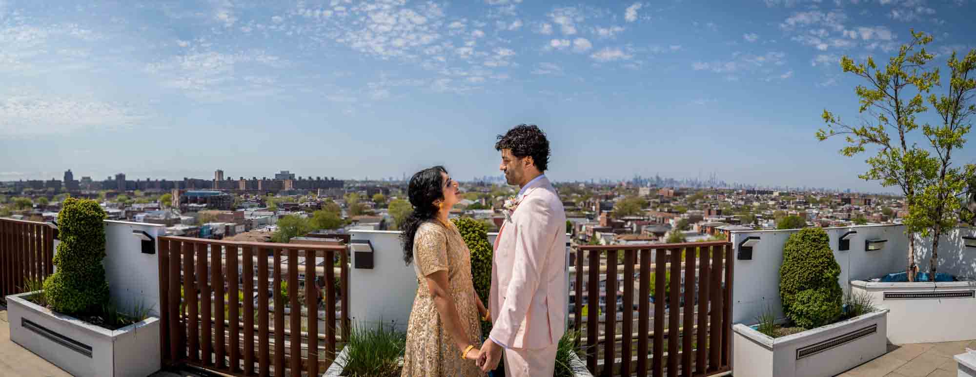 Panorama shot of Indian bride and groom holding hands on roof with view of Manhattan in background during a Terrace on the Park wedding