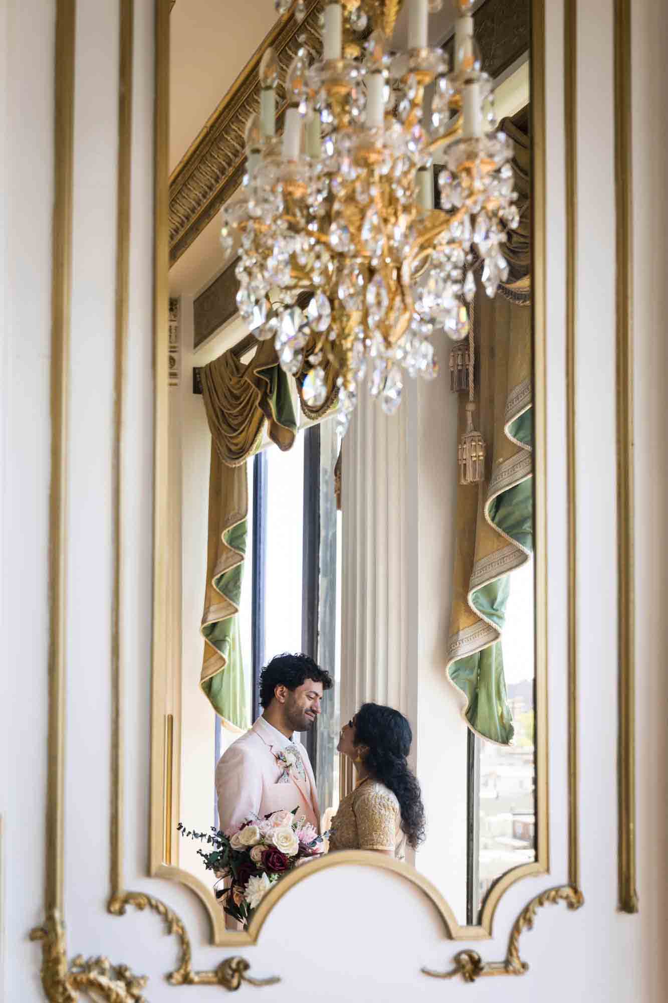 Reflection of Indian bride and groom looking at each other under chandelier during a Terrace on the Park wedding