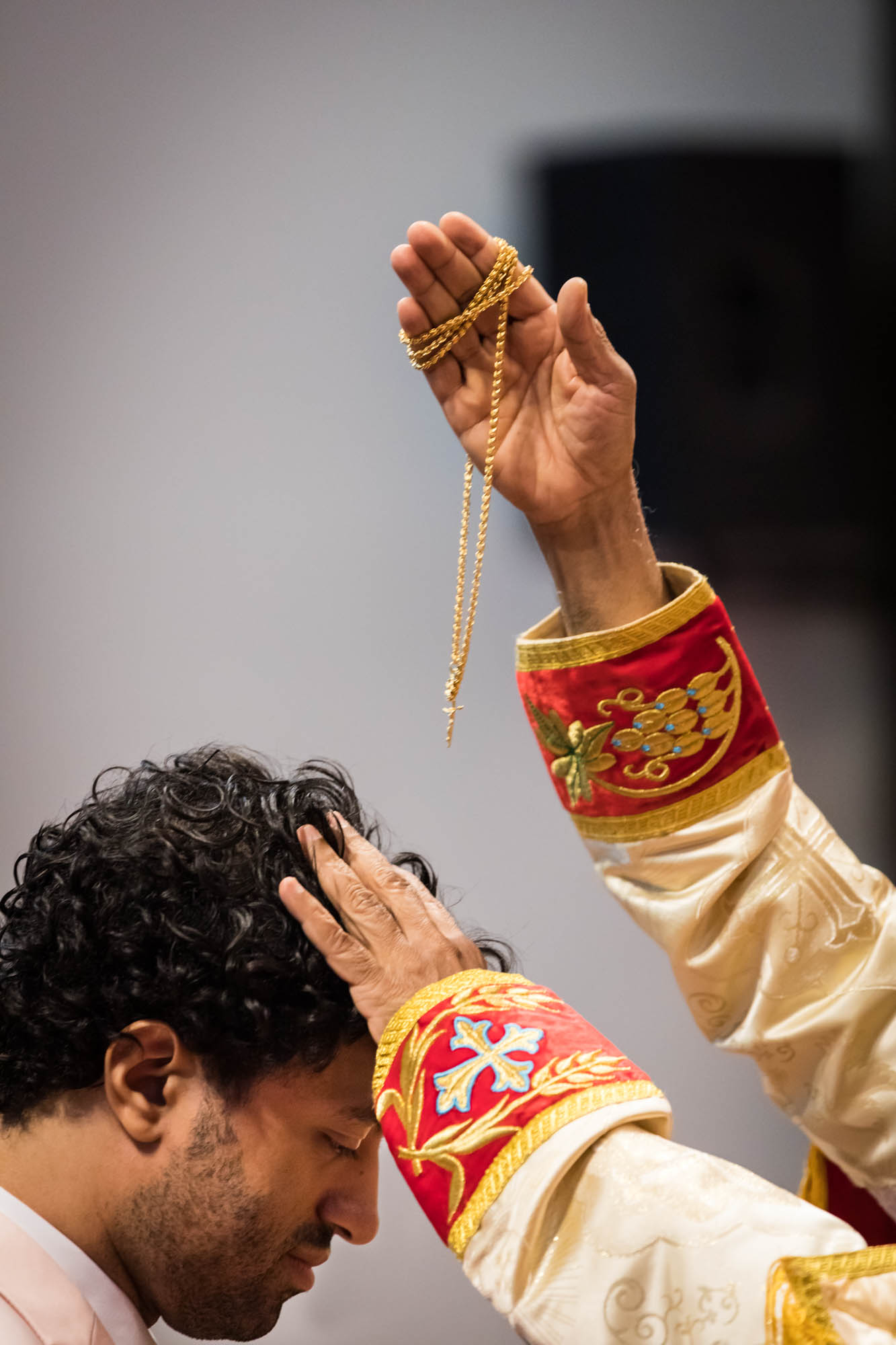 Priest blessing groom with a gold necklace during Syro-Malankara Catholic wedding ceremony
