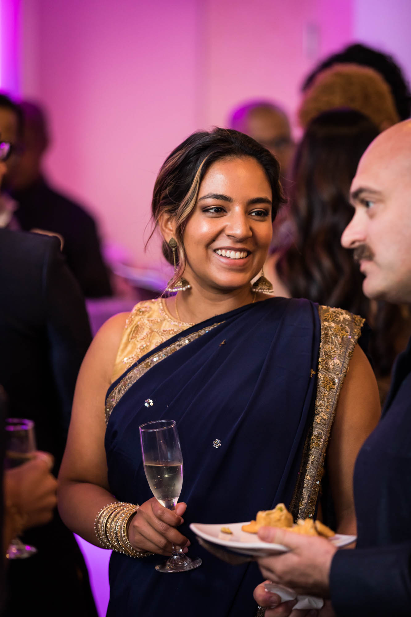 Woman wearing navy and gold sari during holding a glass of champagne a Terrace on the Park wedding