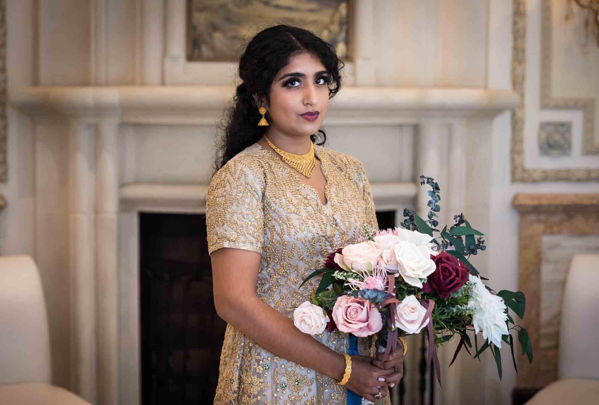 Indian bride wearing gold dress holding flower bouquet during a Terrace on the Park wedding
