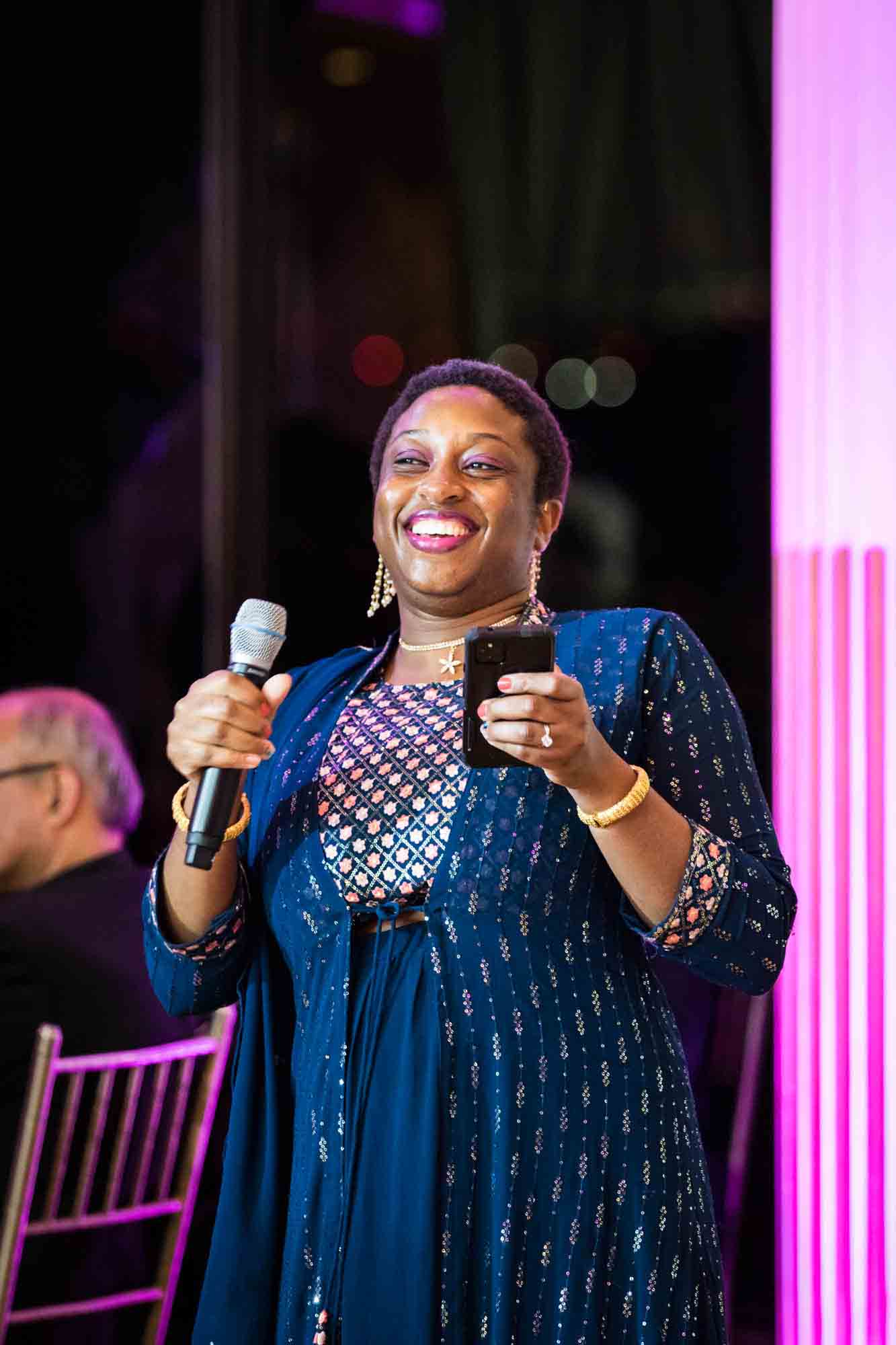 African American woman wearing Indian dress holding microphone and cell phone during speeches during a Terrace on the Park wedding