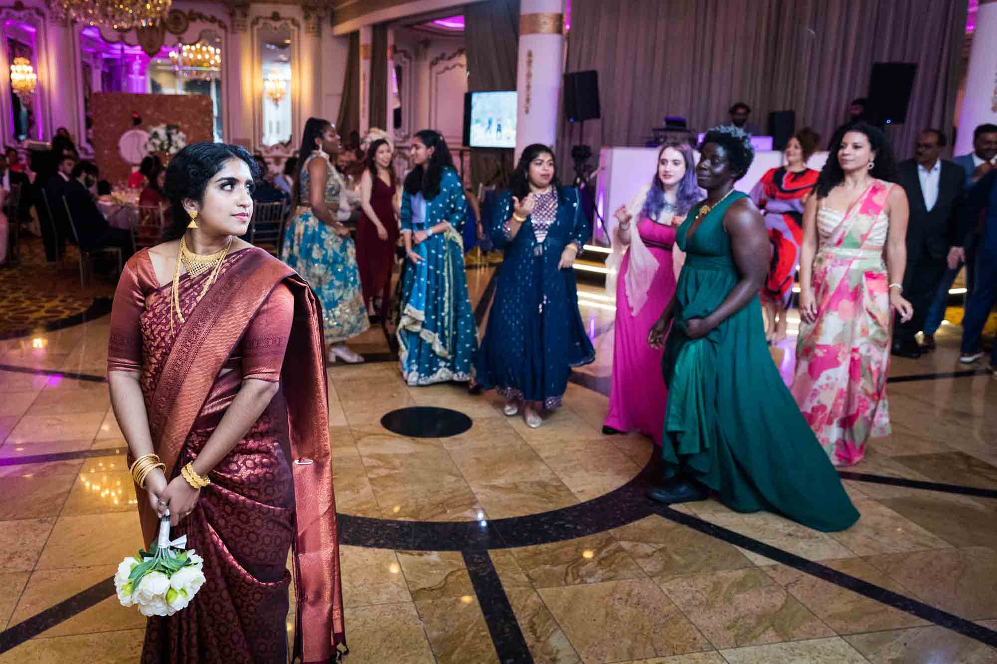 Indian bride in rust colored sari holding bouquet about to toss flowers to female guests for an article on Terrace on the Park wedding photo tips