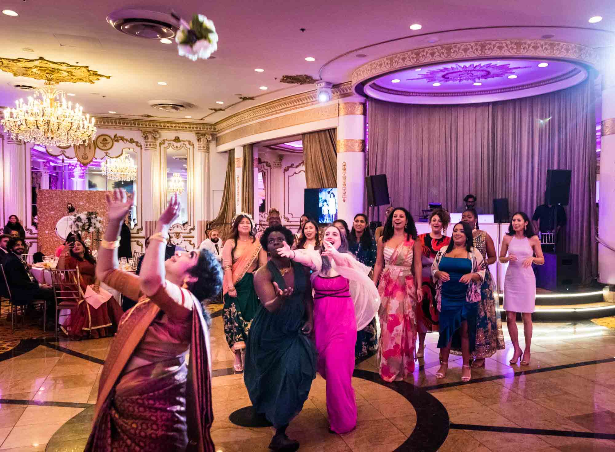 Indian bride throwing bouquet in the air and female guests running to catch bouquet on dance floor for an article on Terrace on the Park wedding photo tips