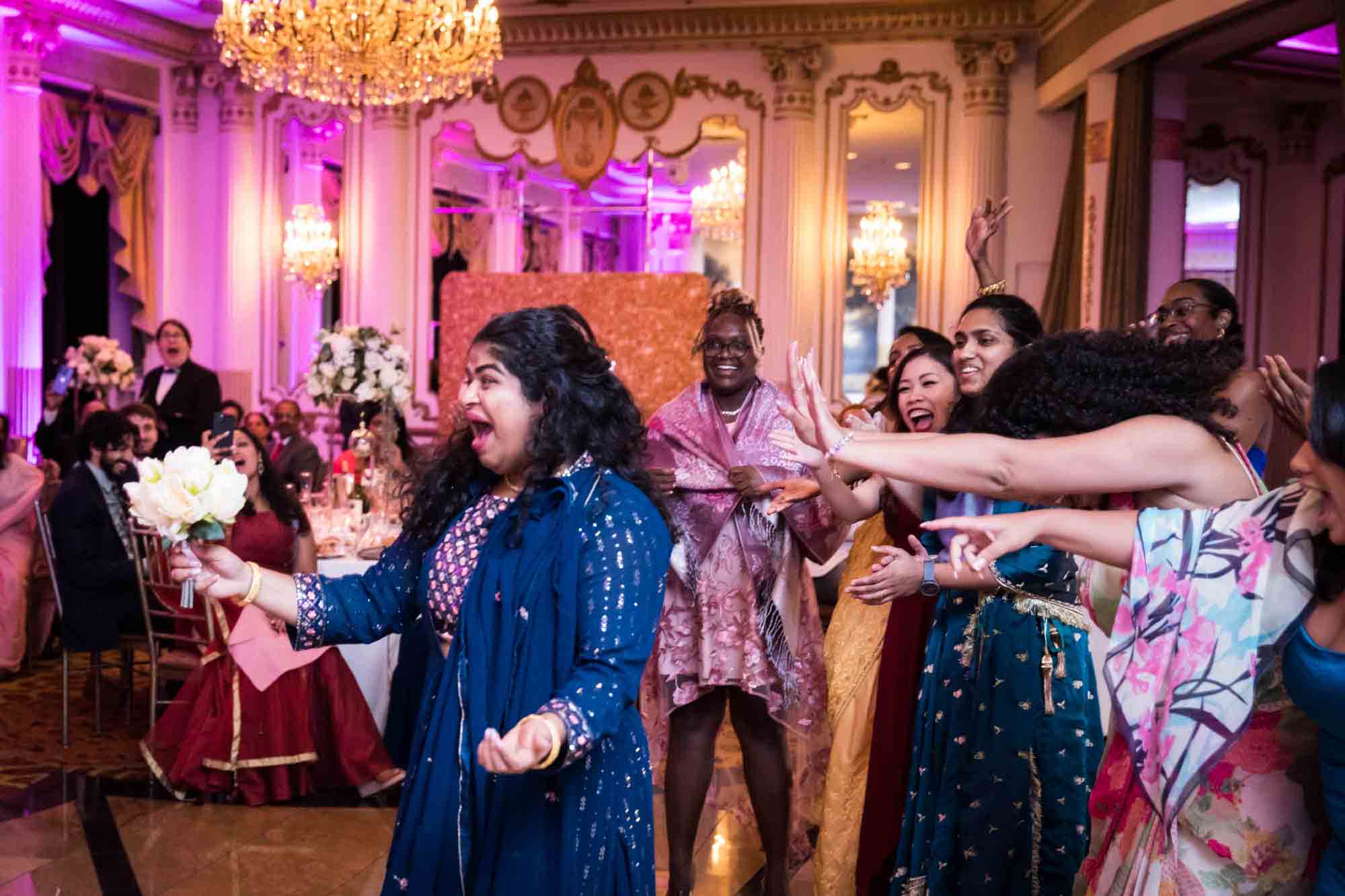 Bridesmaid in blue sari catching bouquet with female guests reacting for an article on Terrace on the Park wedding photo tips