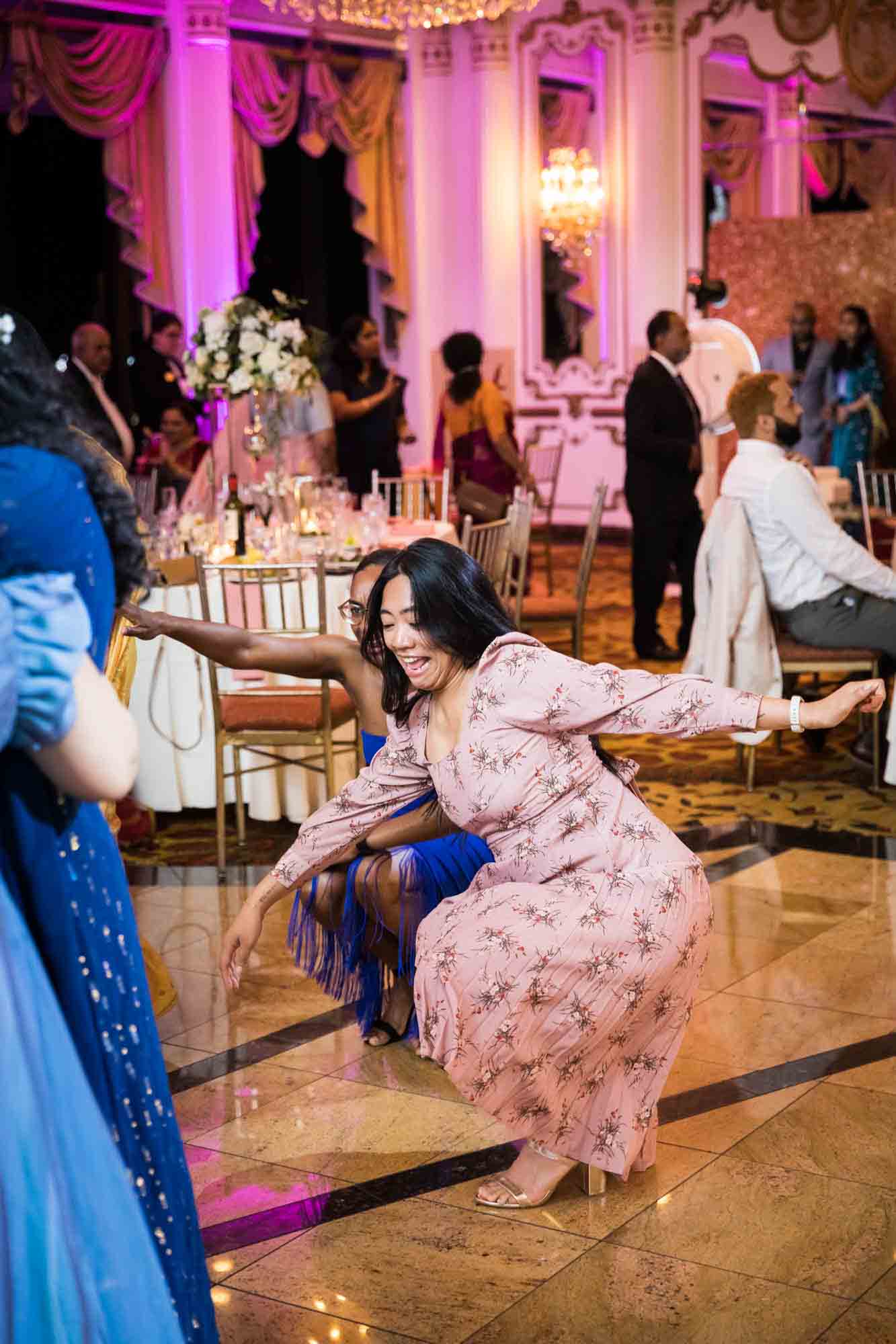 Asian and black women dancing in crouched position on dance floor for an article on Terrace on the Park wedding photo tips