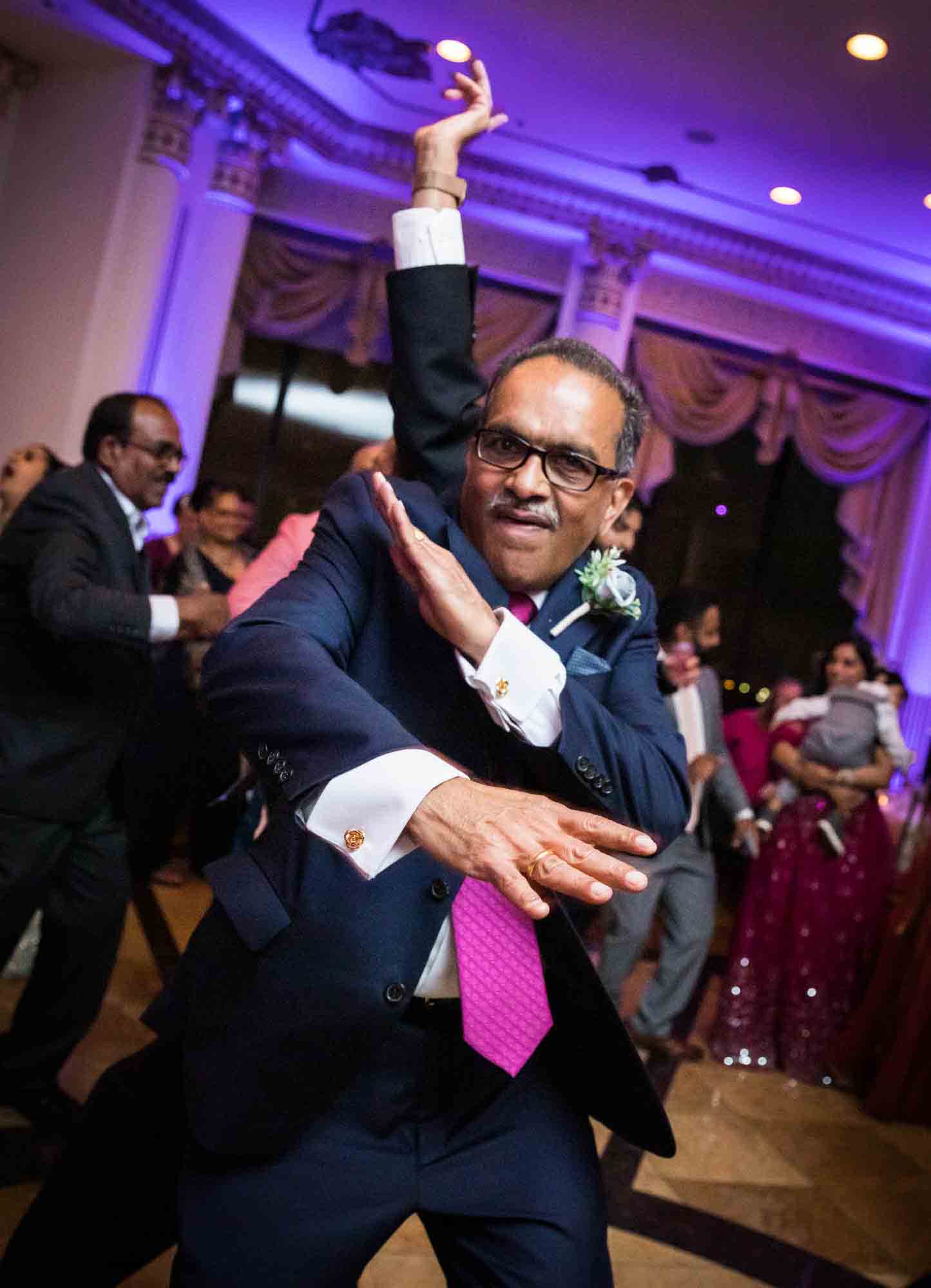 Man wearing blue suit and pink tie dancing for an article on Terrace on the Park wedding photo tips