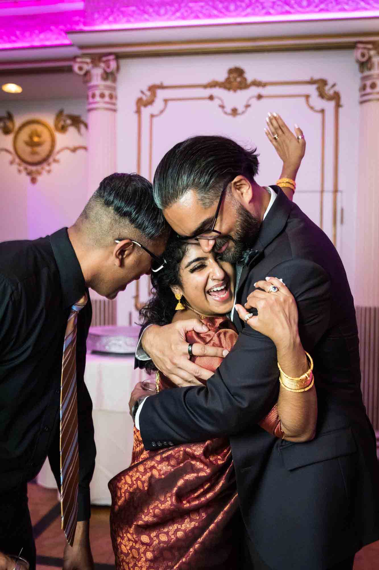 Bride being embraced by two male friends for an article on Terrace on the Park wedding photo tips