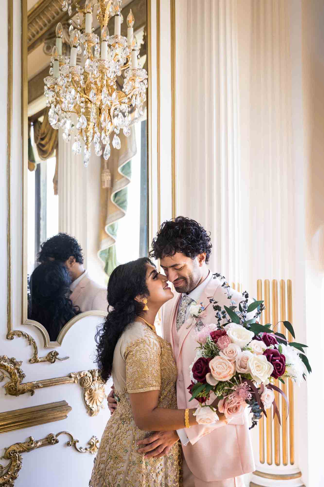 Indian bride and groom about to kiss in front of mirror and chandelier during a Terrace on the Park wedding