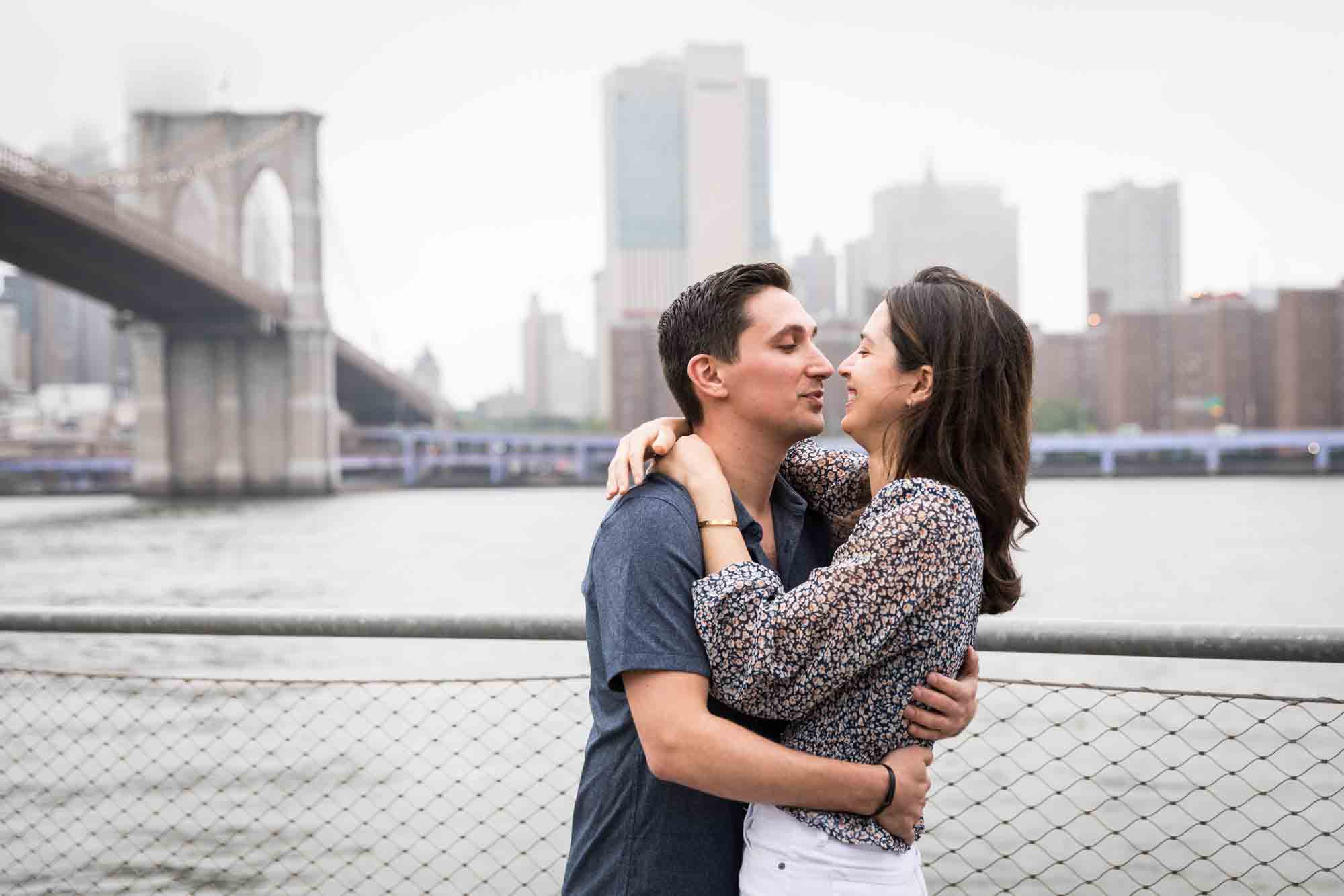 Couple about to kiss in front of waterfront and Brooklyn Bridge after a Brooklyn Bridge Park surprise proposal