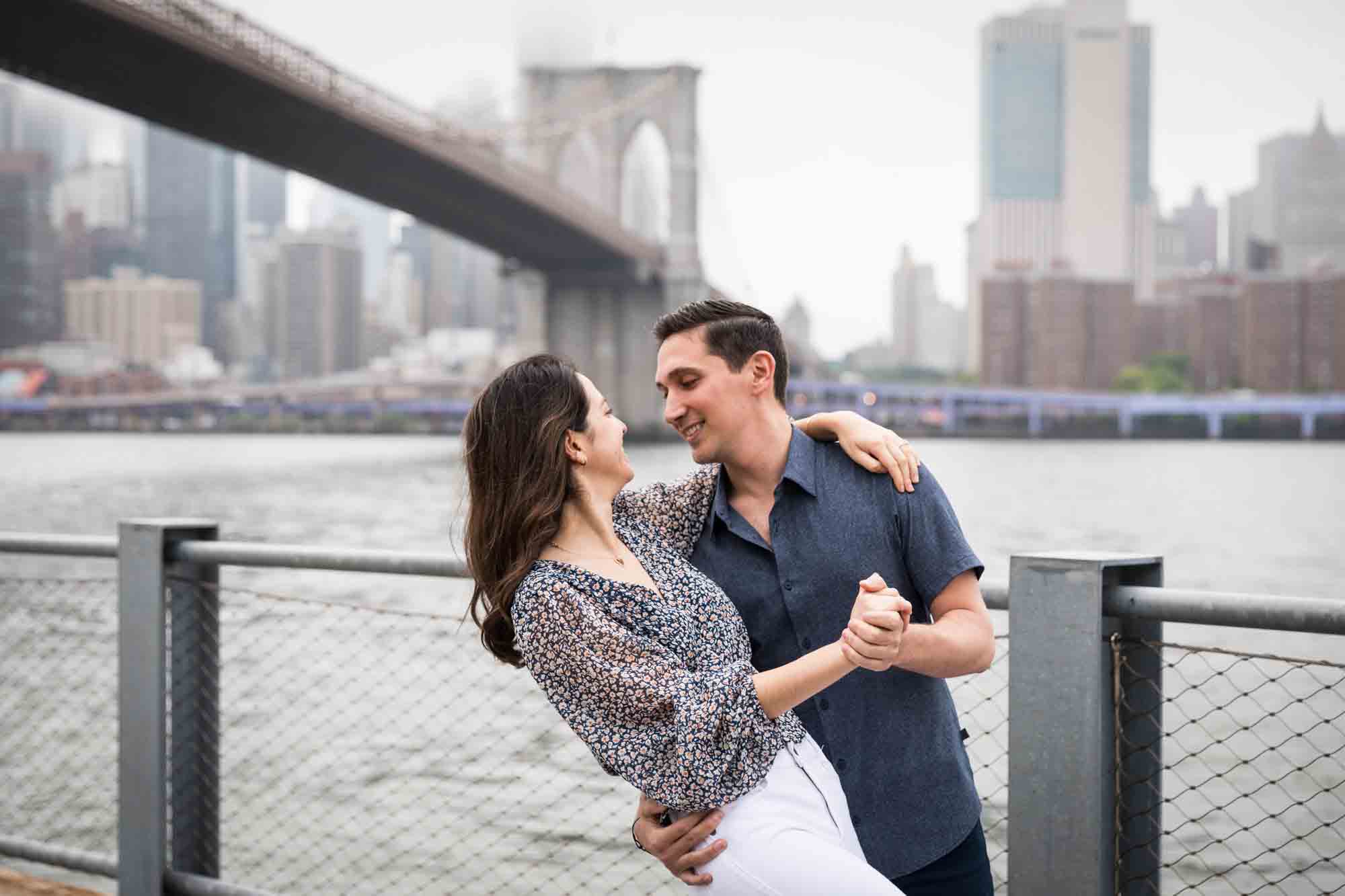 Couple dancing in front of NYC waterfront and Brooklyn Bridge after a Brooklyn Bridge Park surprise proposal