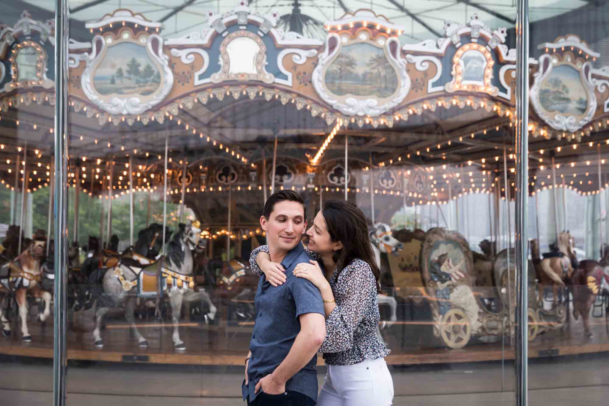 Couple hugging in front of Jane's Carousel after a Brooklyn Bridge Park surprise proposal