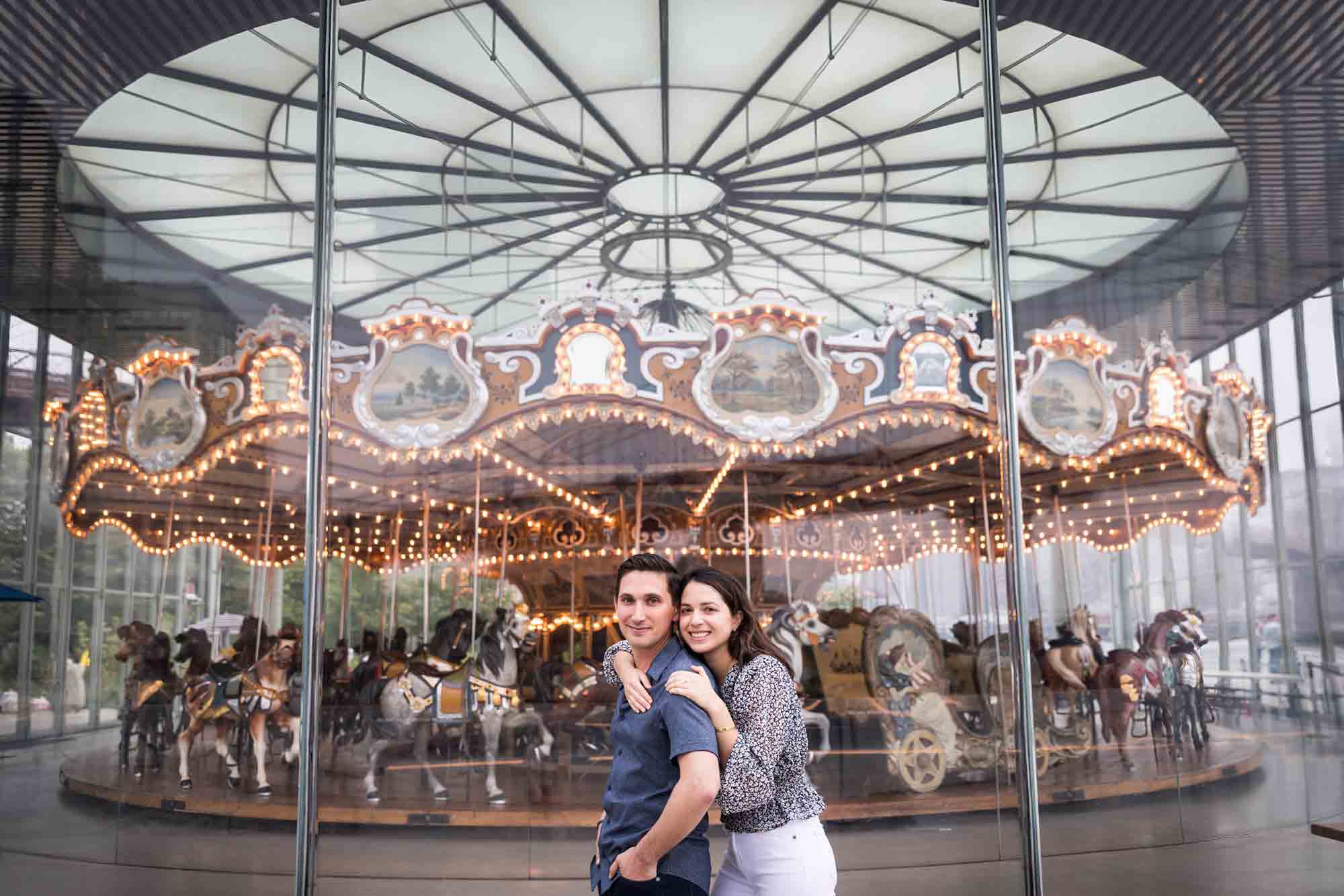 Couple hugging in front of Jane's Carousel after a Brooklyn Bridge Park surprise proposal