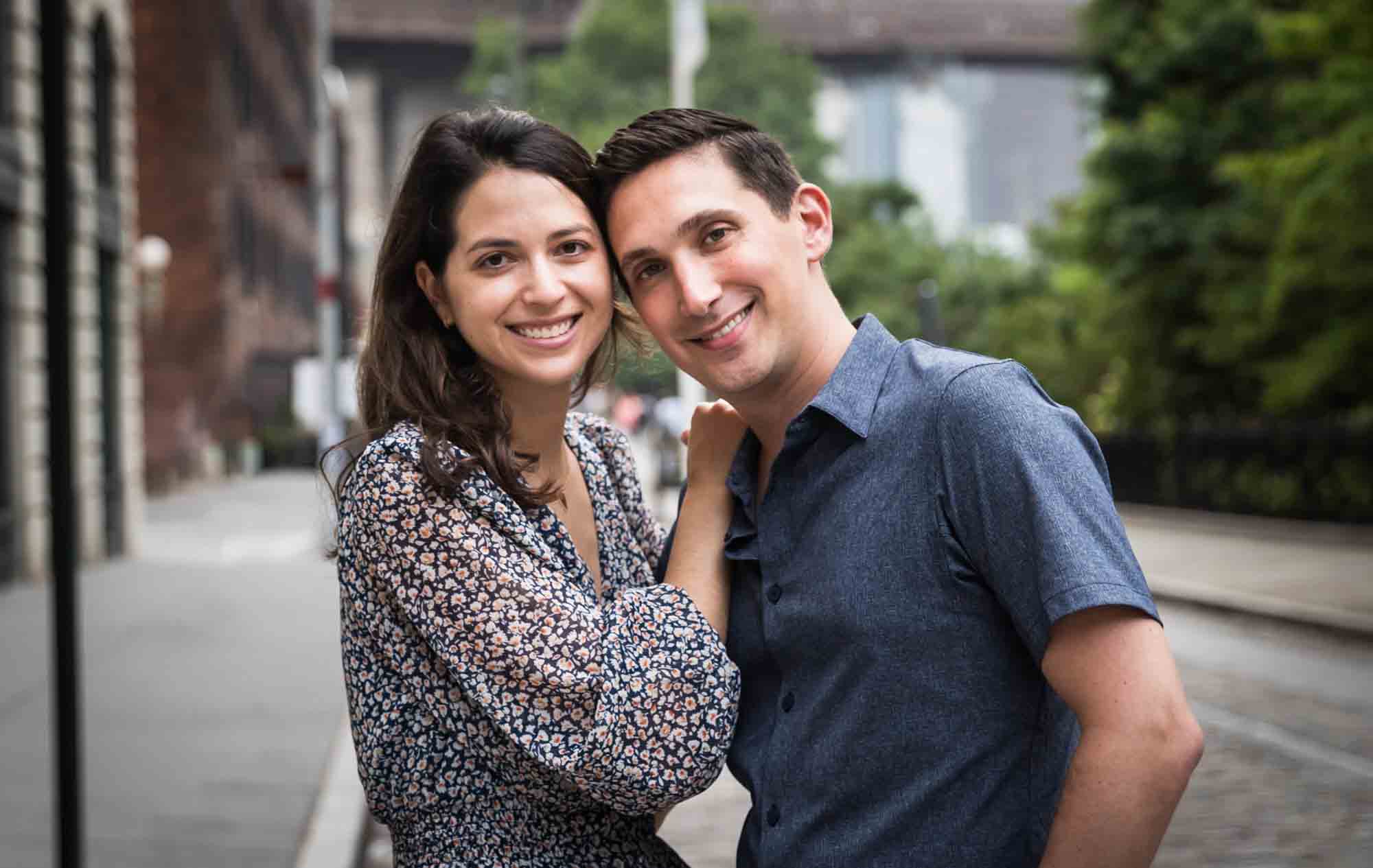 Couple hugging in middle of cobblestone street after a Brooklyn Bridge Park surprise proposal