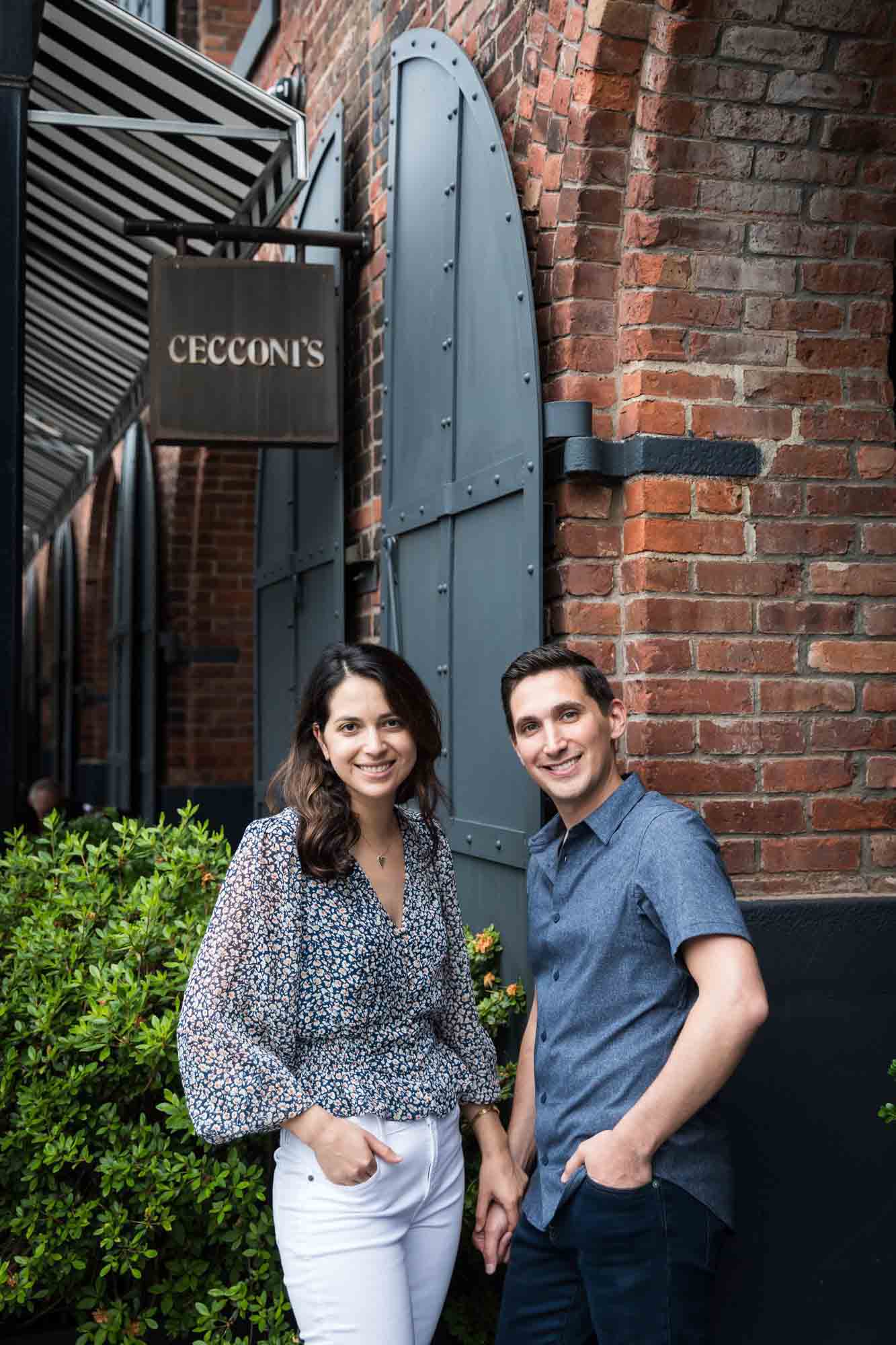 Couple holding hands in front of Cecconi's restaurant sign in Brooklyn Bridge Park