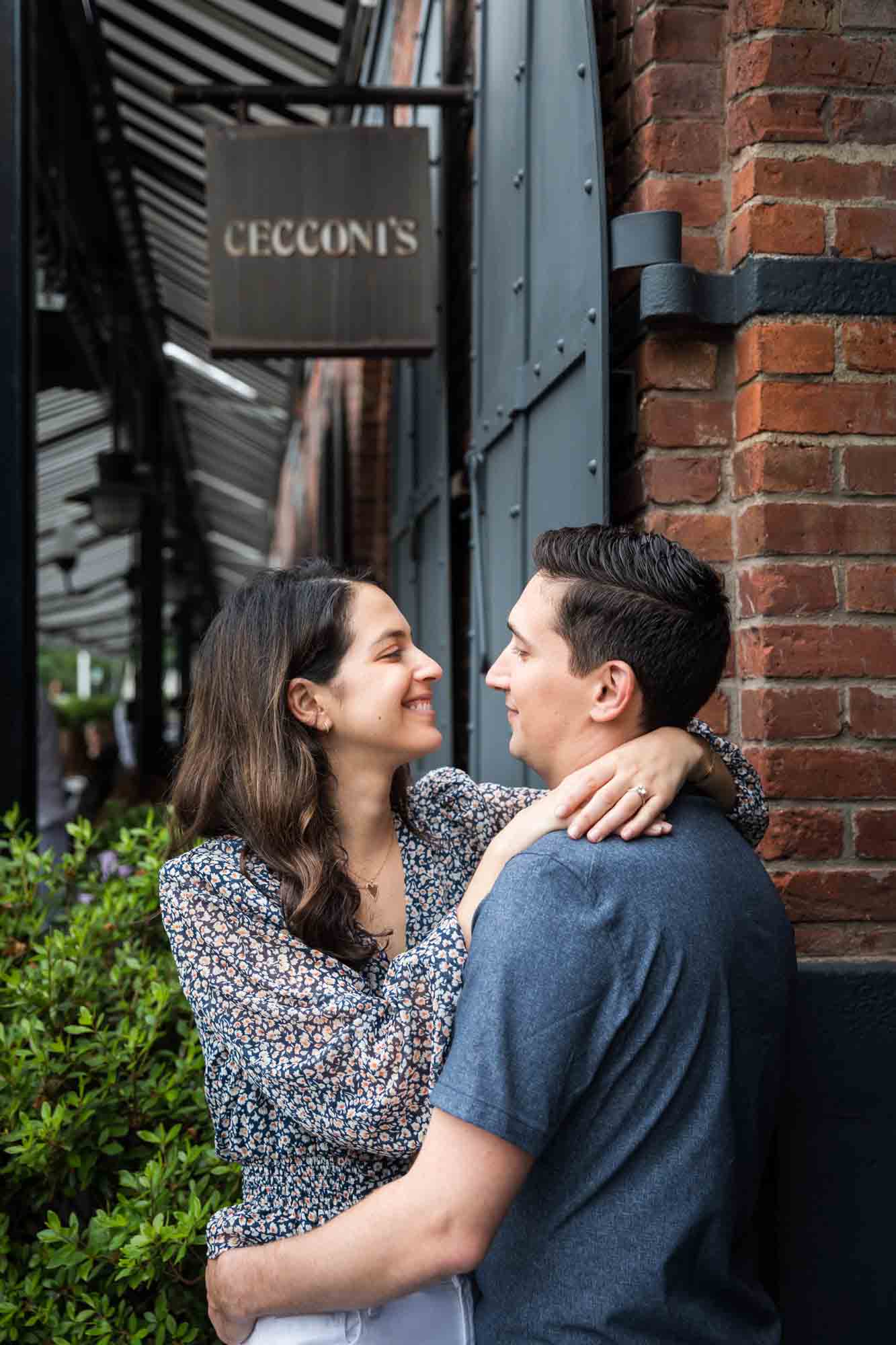 Couple hugging in front of Cecconi's restaurant sign in Brooklyn Bridge Park