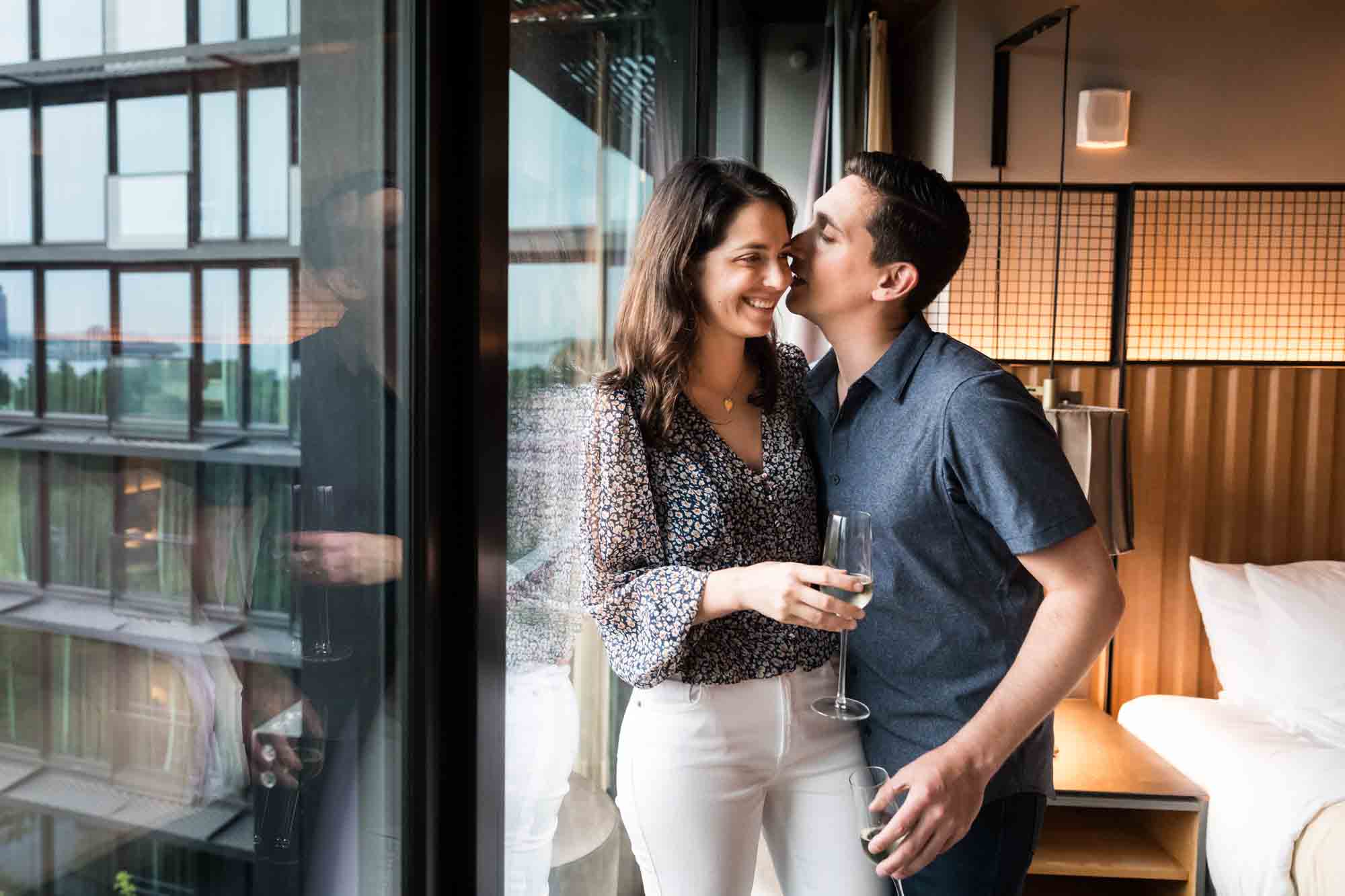 Couple standing together holding champagne glasses in front of hotel room window