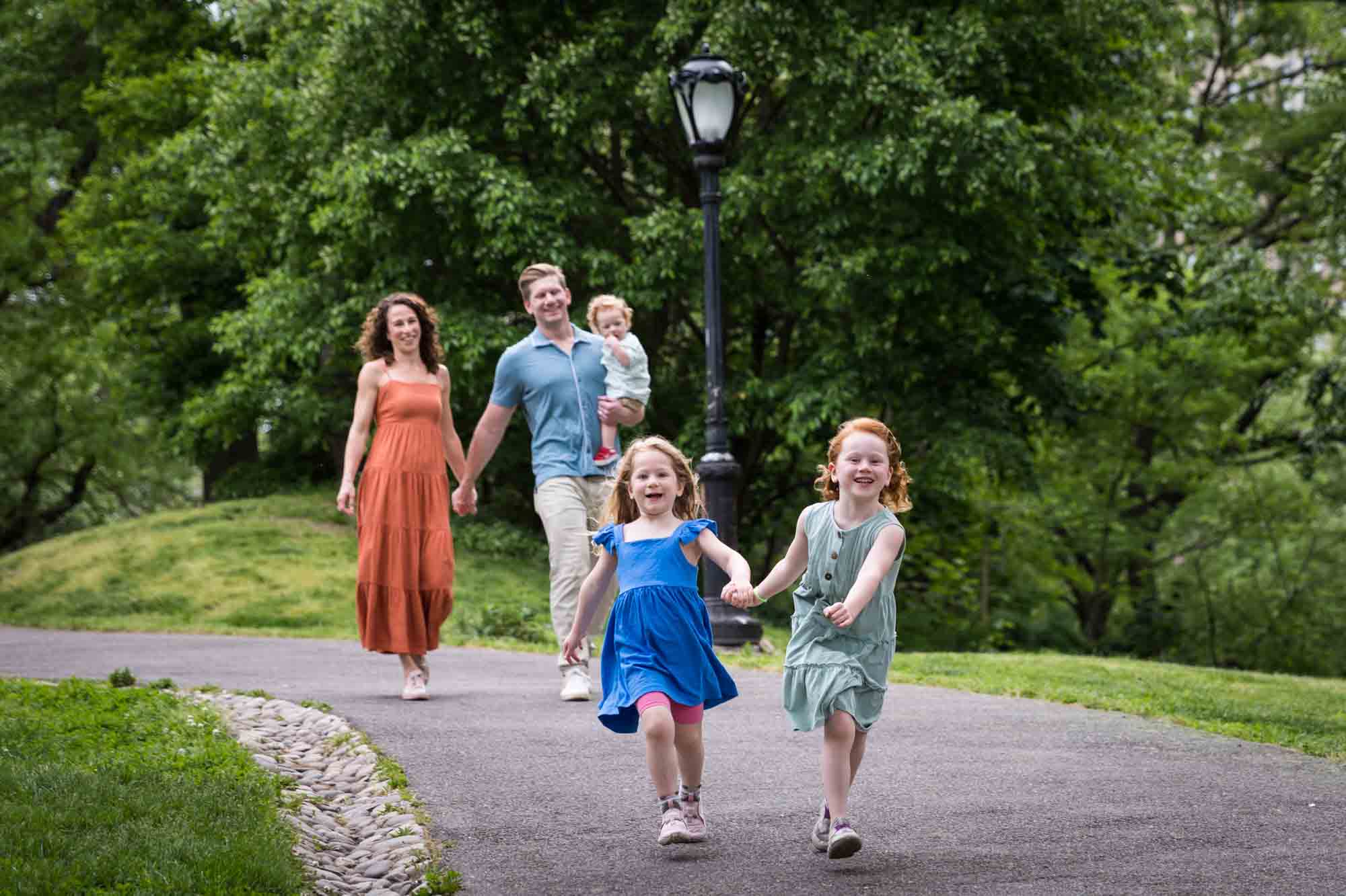 Two little girls holding hands wearing blue dresses running down pathway during a Central Park family portrait session