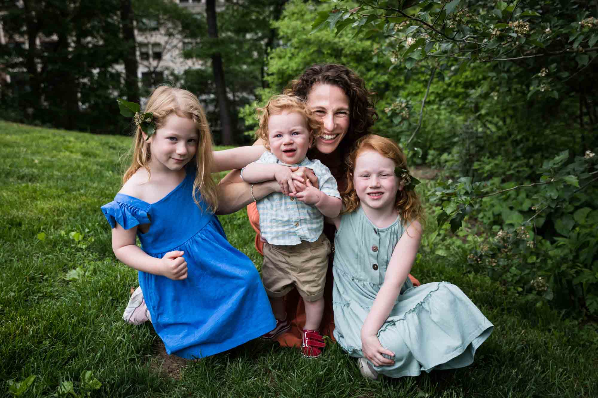 Mother with three children sitting in grass in front of bush during a Central Park family portrait session