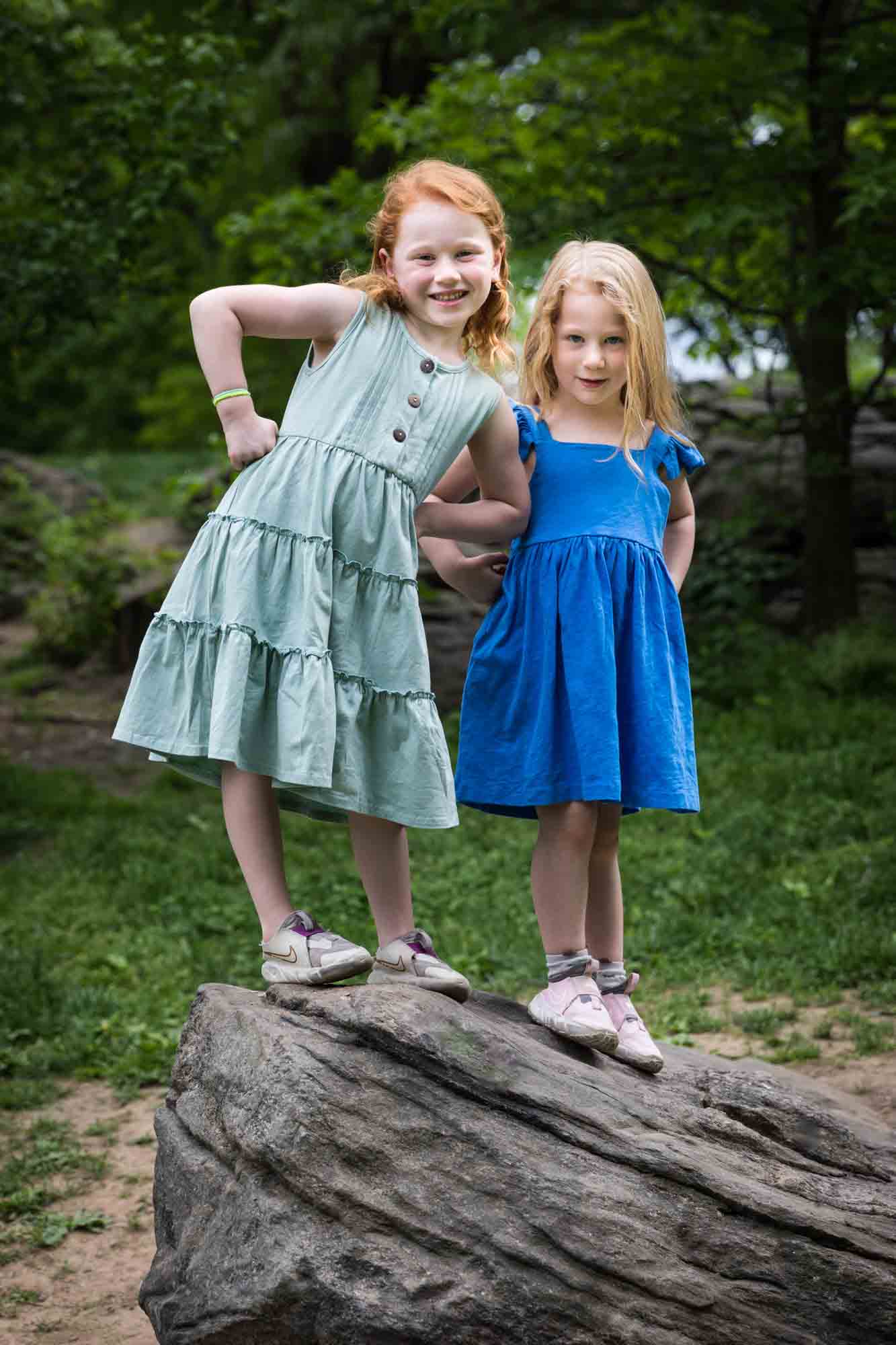 Two little girls wearing blue dresses standing on rock during a Central Park family portrait session