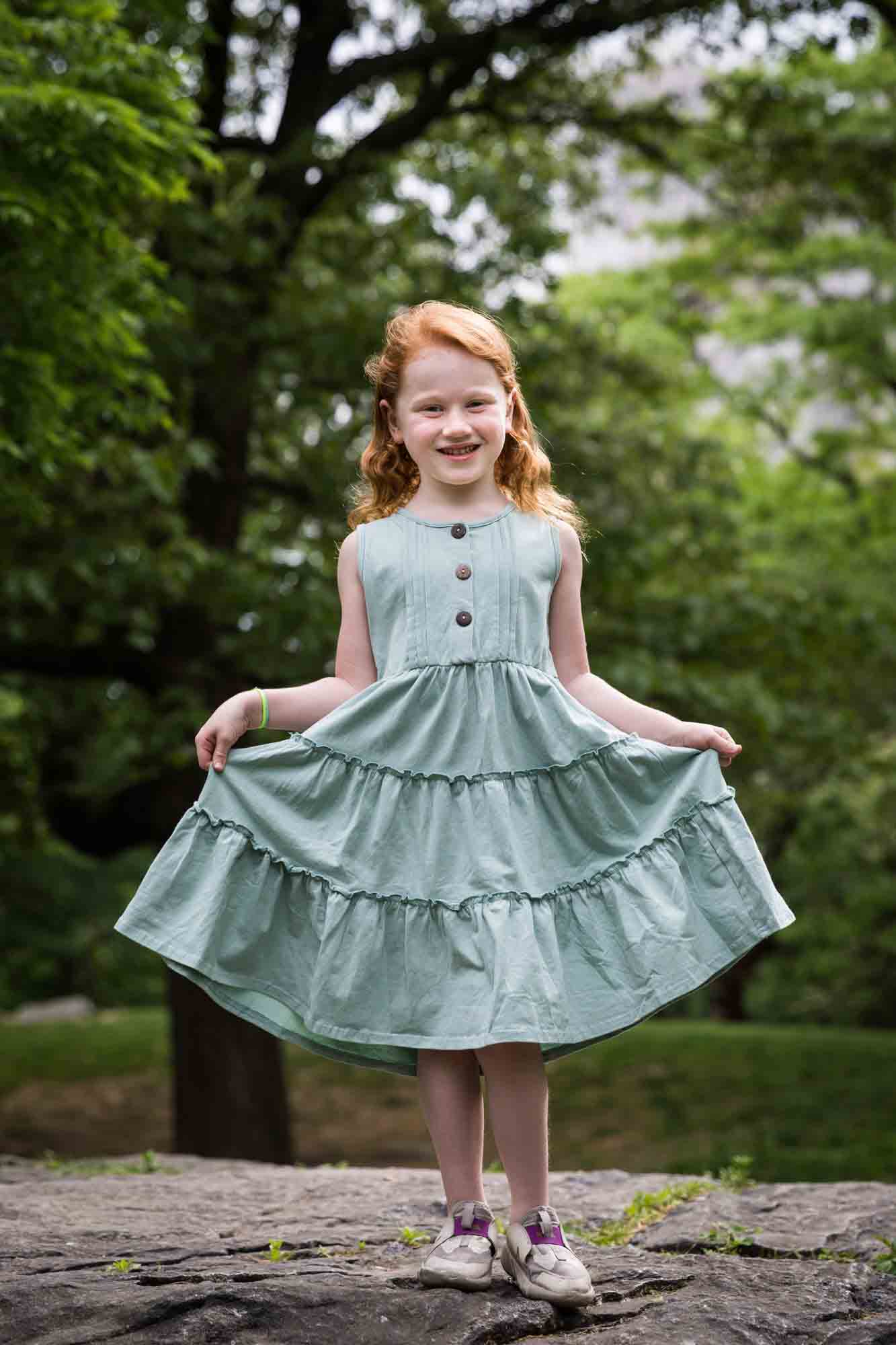 Little red-haired girl wearing green dress dancing on rock during a Central Park family portrait session
