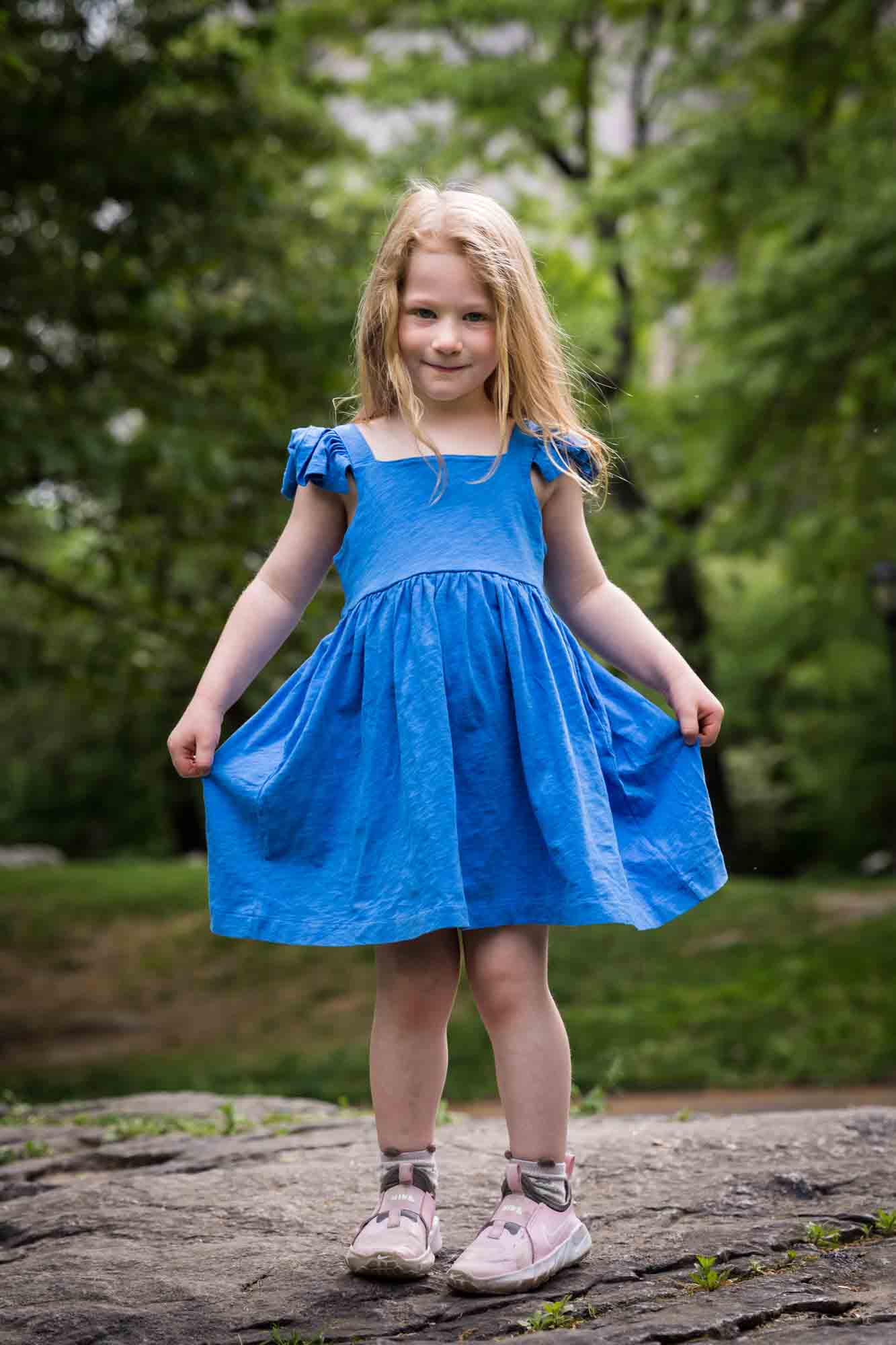 Little girl wearing blue dress dancing on rock during a Central Park family portrait session