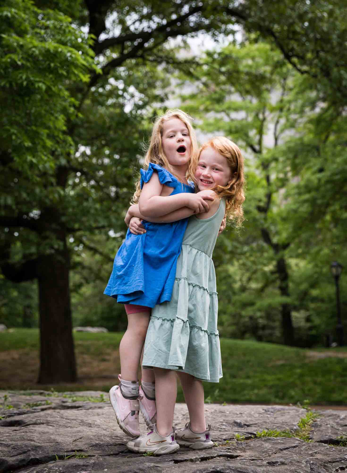 Two little girls wearing blue dresses hugging on rock during a Central Park family portrait session