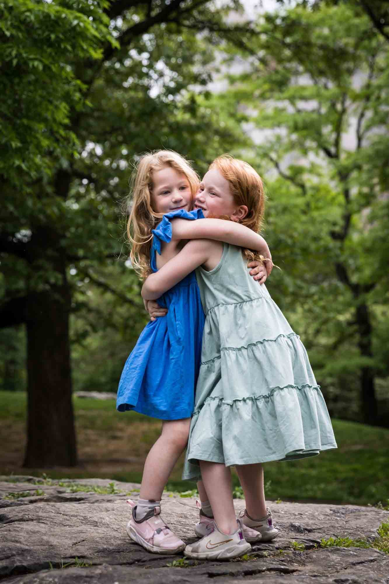 Two little girls wearing blue dresses hugging on rock during a Central Park family portrait session